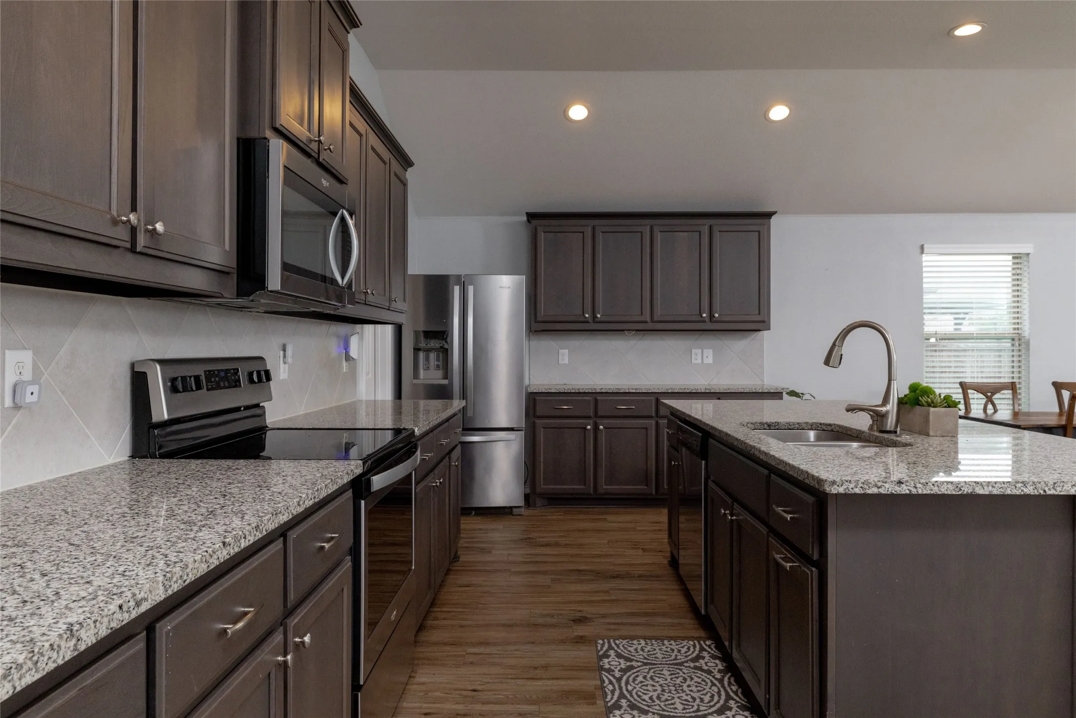 Kitchen featuring stainless steel appliances, light stone countertops, backsplash, dark wood-style floors, and recessed lighting
