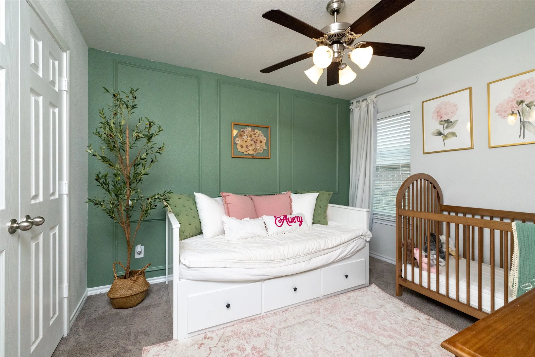 Bedroom with a decorative wall, light colored carpet, a ceiling fan, and a nursery area