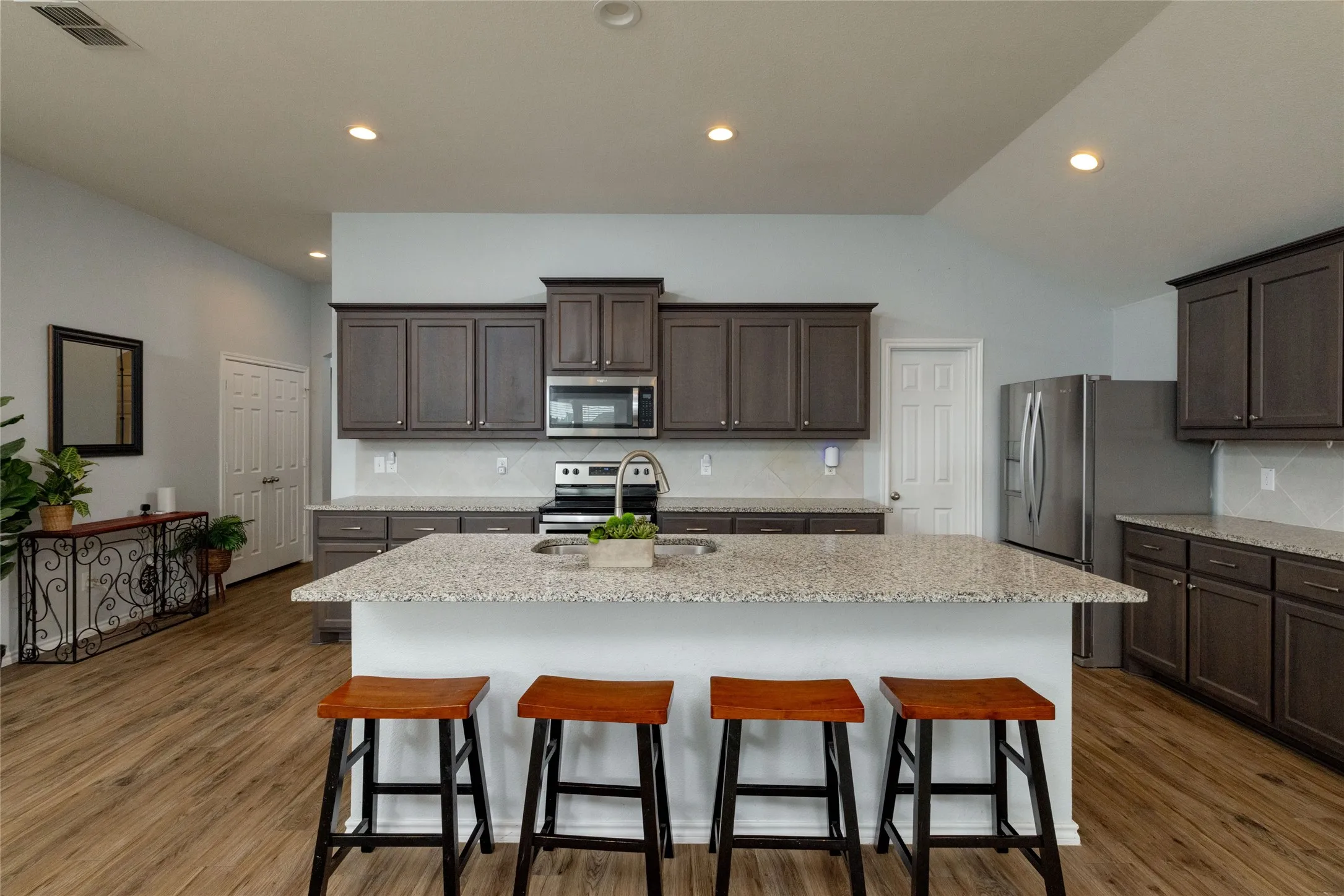 Kitchen featuring dark wood finish cabinetry, a kitchen breakfast bar, stainless steel appliances, light stone counters, and a center island with sink
