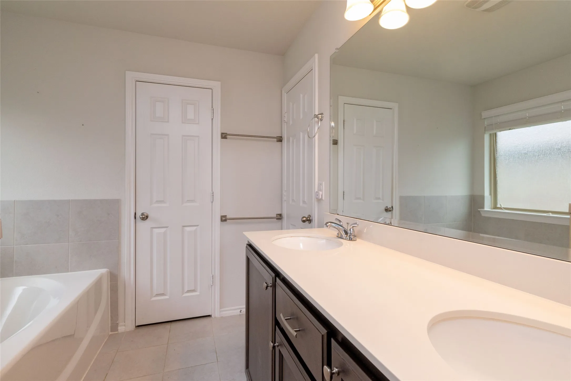 Bathroom featuring a bath, double vanity, and light tile patterned floors