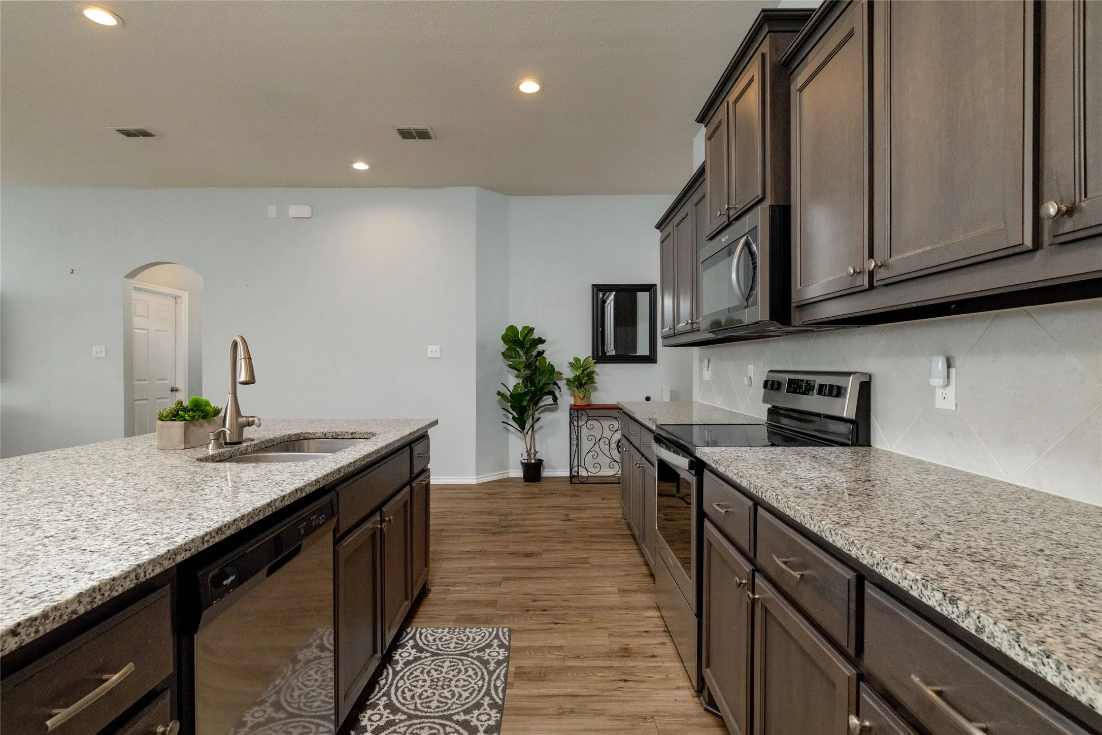Kitchen featuring arched walkways, stainless steel appliances, dark wood finish cabinetry, and recessed lighting