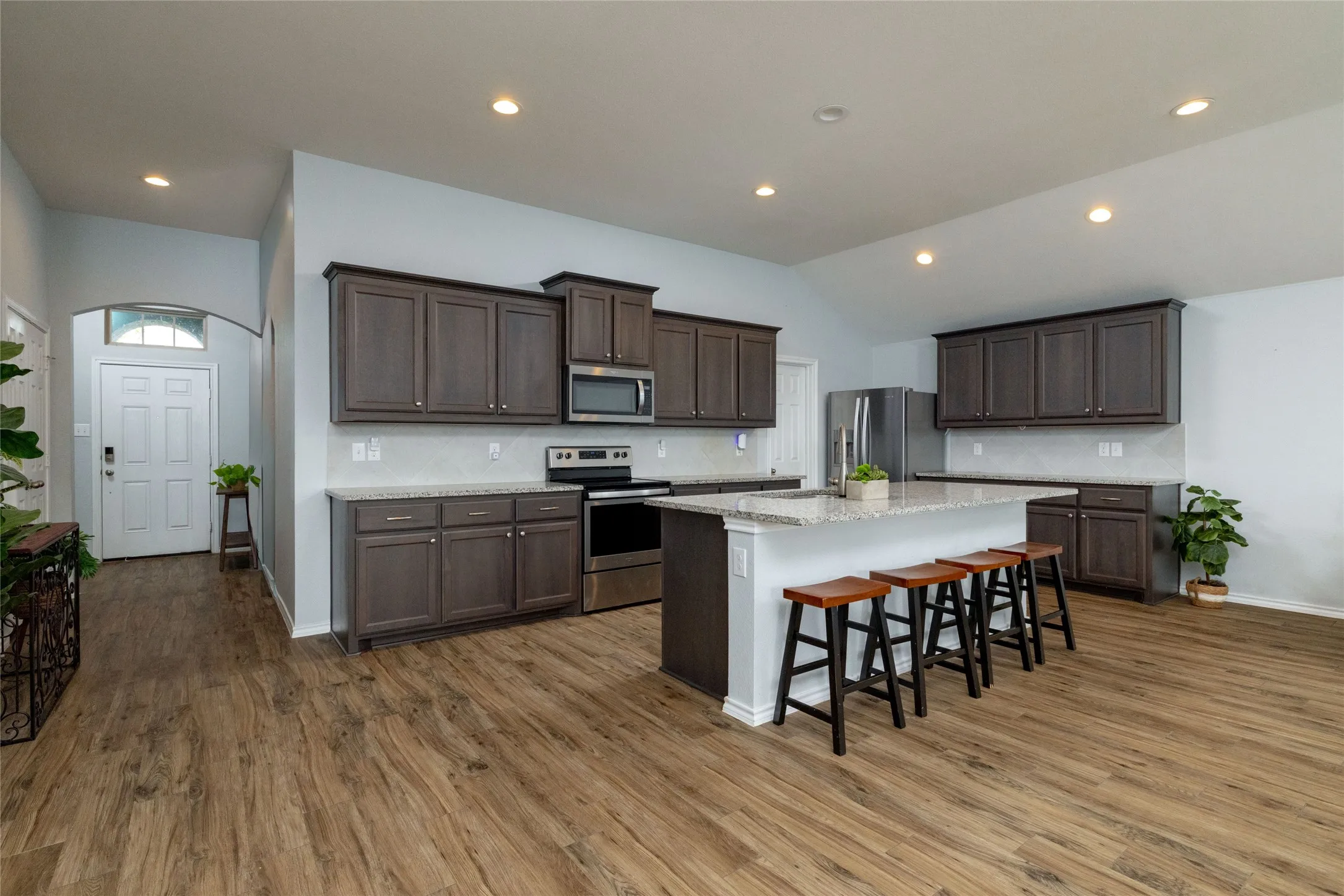 Kitchen featuring dark wood finish cabinets, stainless steel appliances, a breakfast bar area, an island with sink, and vaulted ceiling