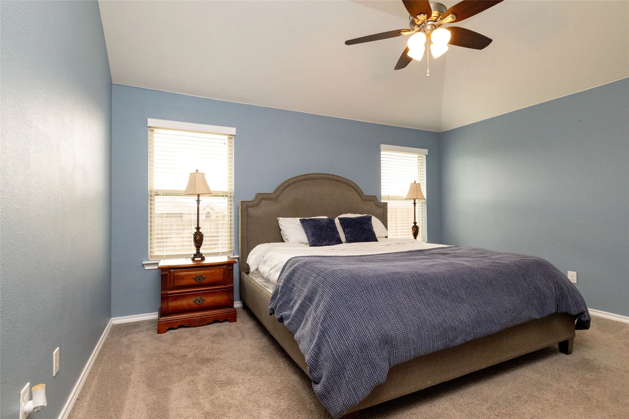 Bedroom with multiple windows, light colored carpet, lofted ceiling, and ceiling fan