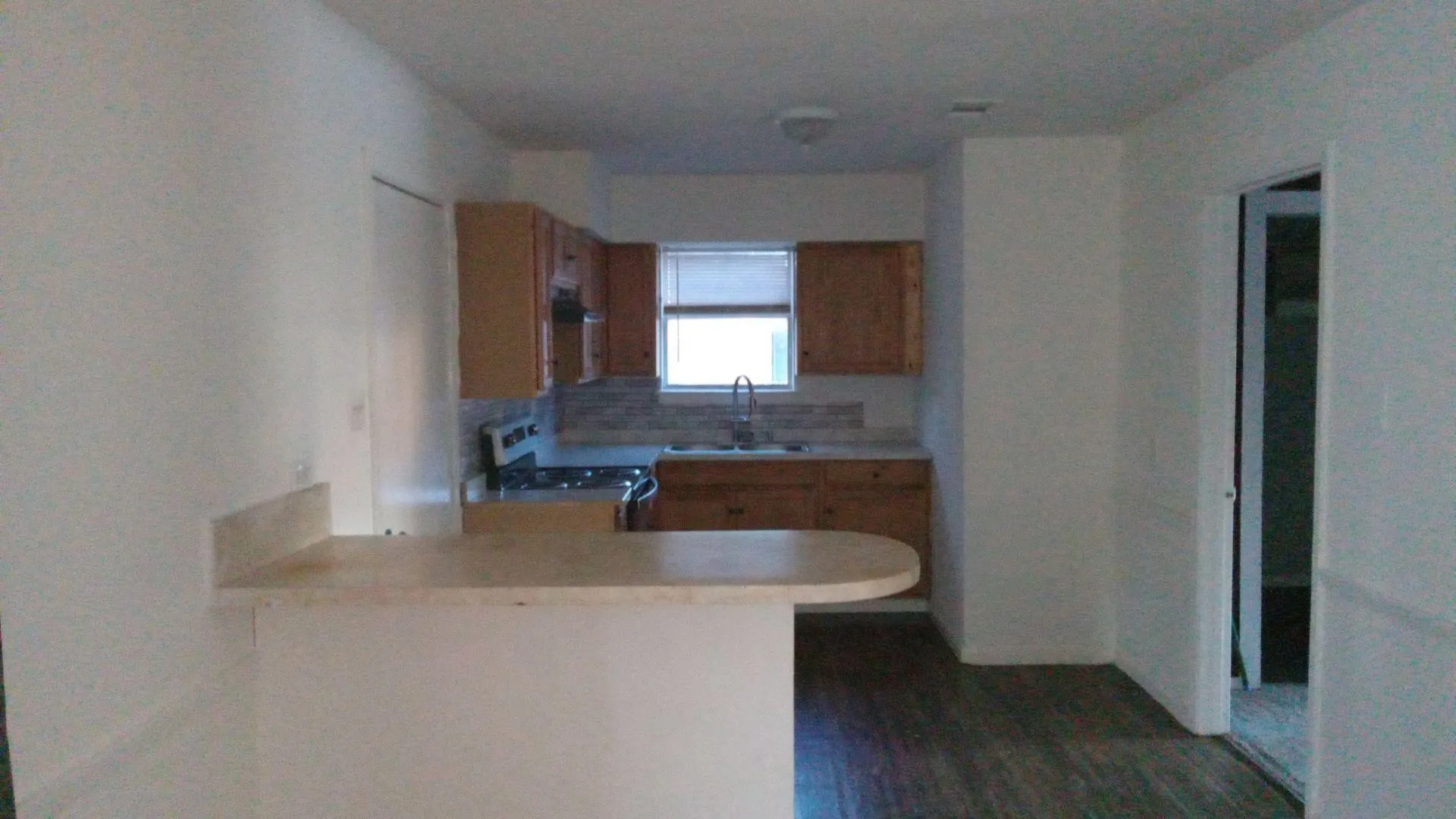 Kitchen featuring light countertops, gas stove, a peninsula, dark wood-style floors, and wood finish cabinets