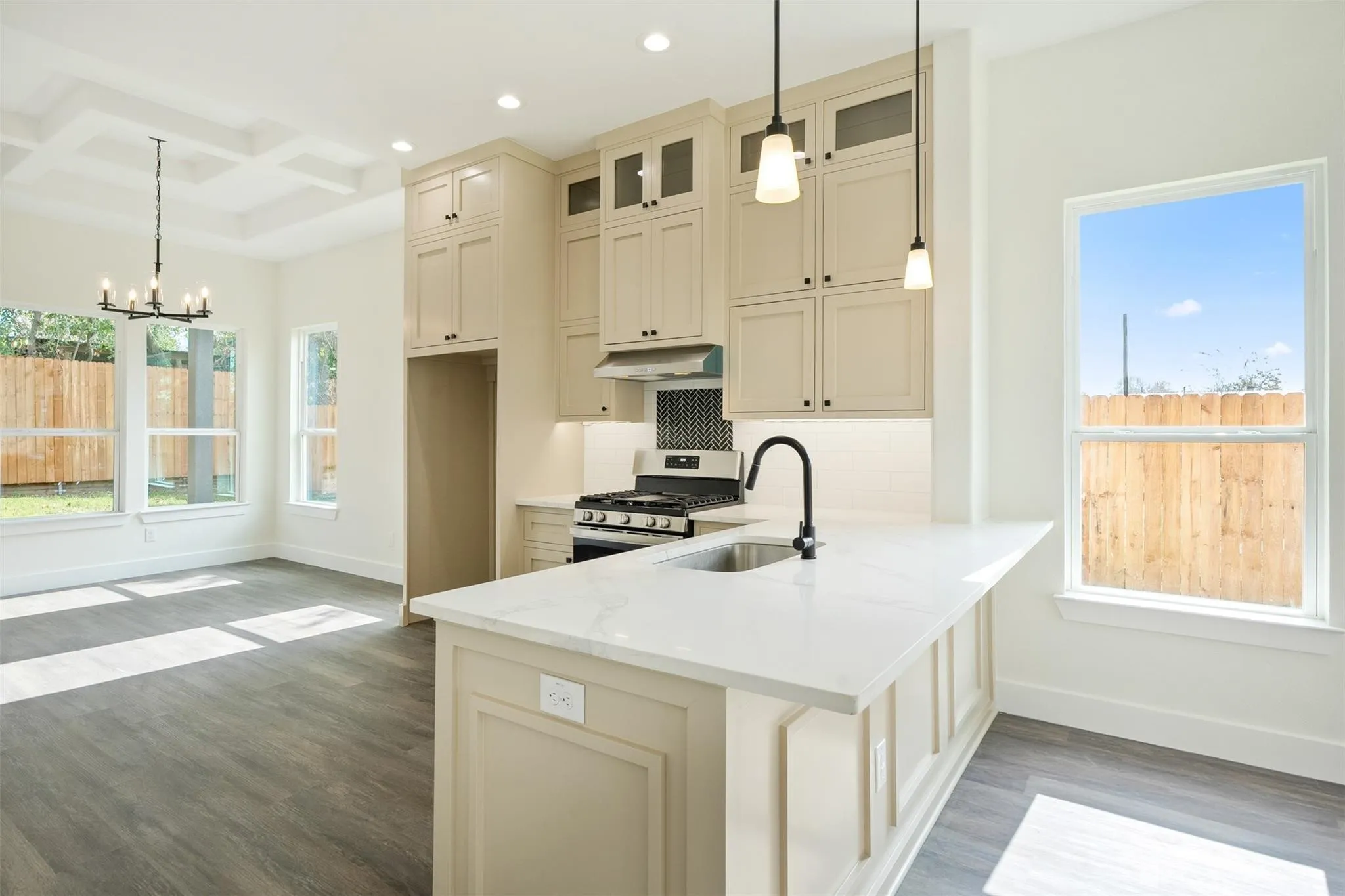 Kitchen featuring cream cabinetry, coffered ceiling, stainless steel gas range, light stone countertops, and dark wood-style floors
