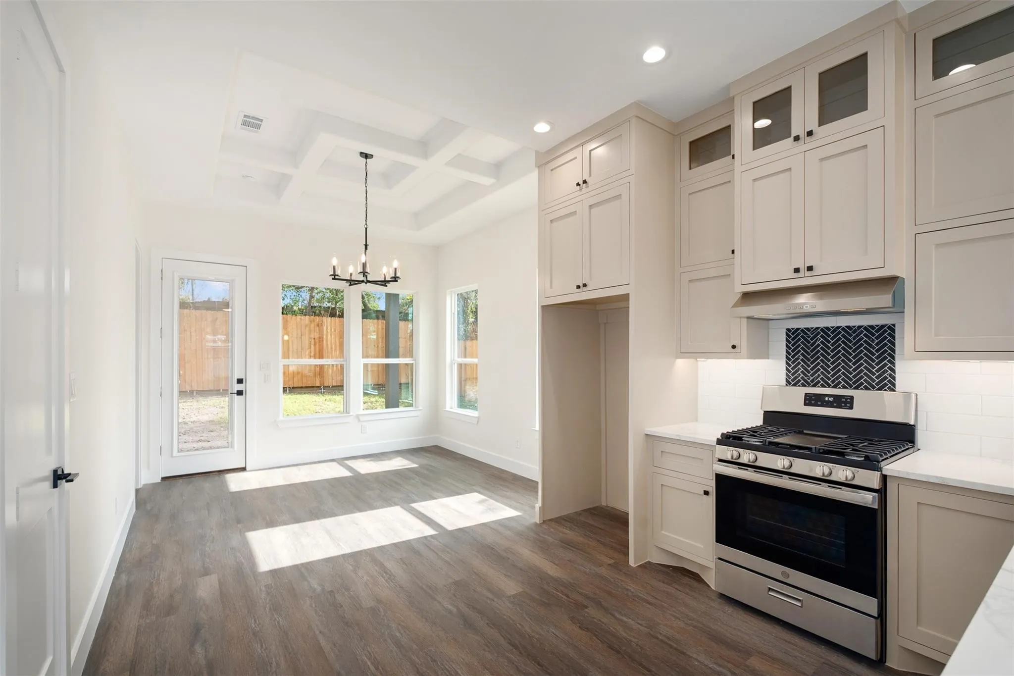 Kitchen with gas range, coffered ceiling, hanging lights, dark wood-type flooring, and decorative backsplash