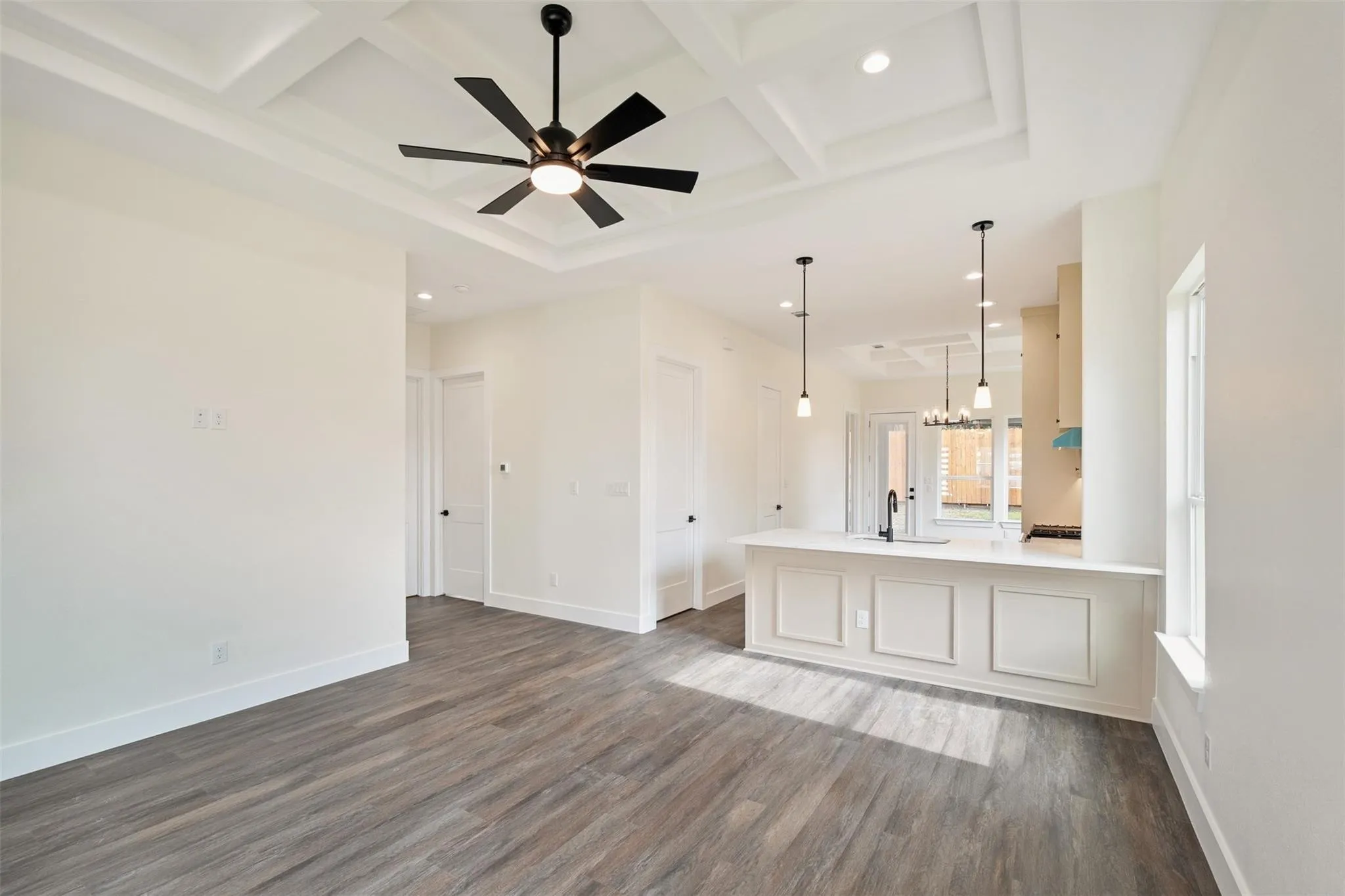 Unfurnished living room with a ceiling fan, coffered ceiling, dark wood finished floors, and hanging lights