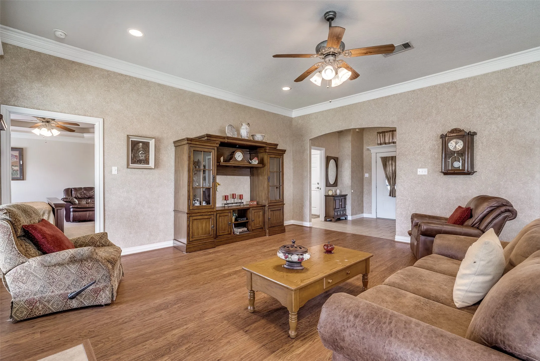 Living room with a ceiling fan, arched walkways, wood finished floors, ornamental molding, and recessed lighting