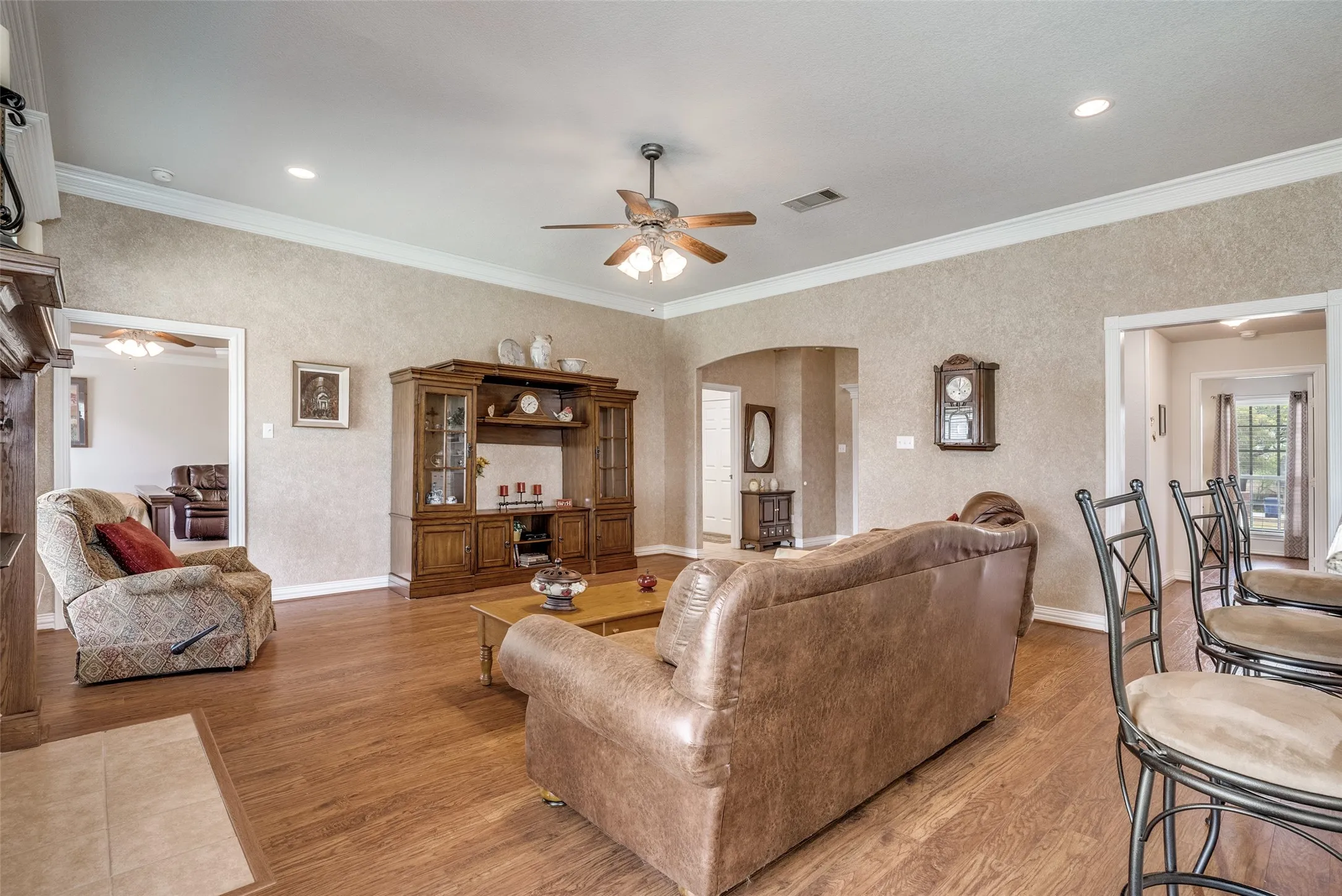 Living room with ornamental molding, a ceiling fan, light wood finished floors, arched walkways, and recessed lighting