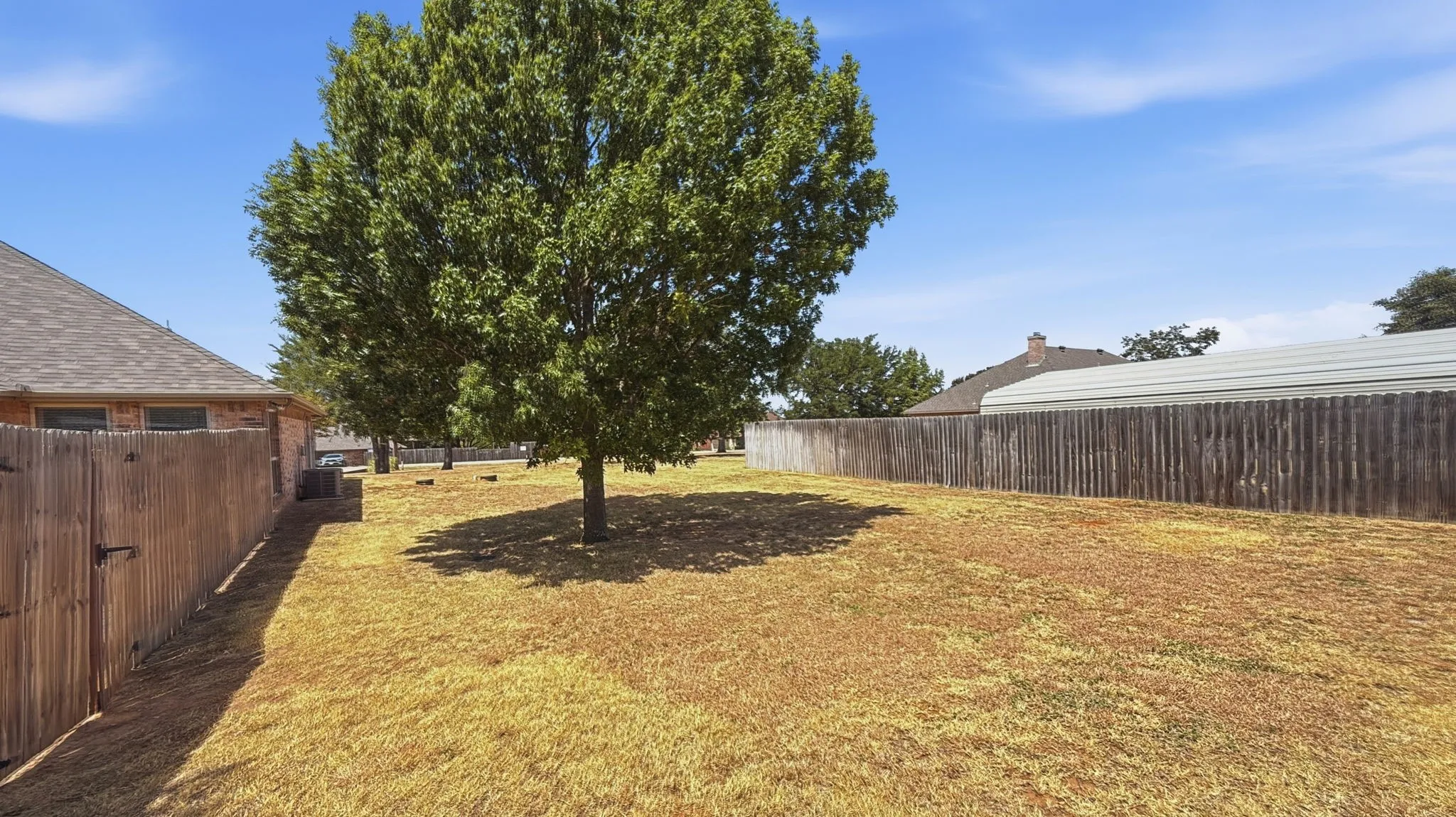 Expansive backyard featuring a mature tree, wood privacy fencing, and a side gate