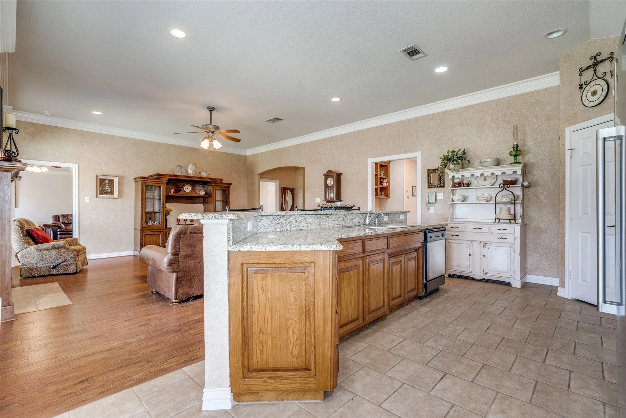 Dual tone kitchen with arched walkways, open floor plan, crown molding, a center island with sink, and light stone countertops