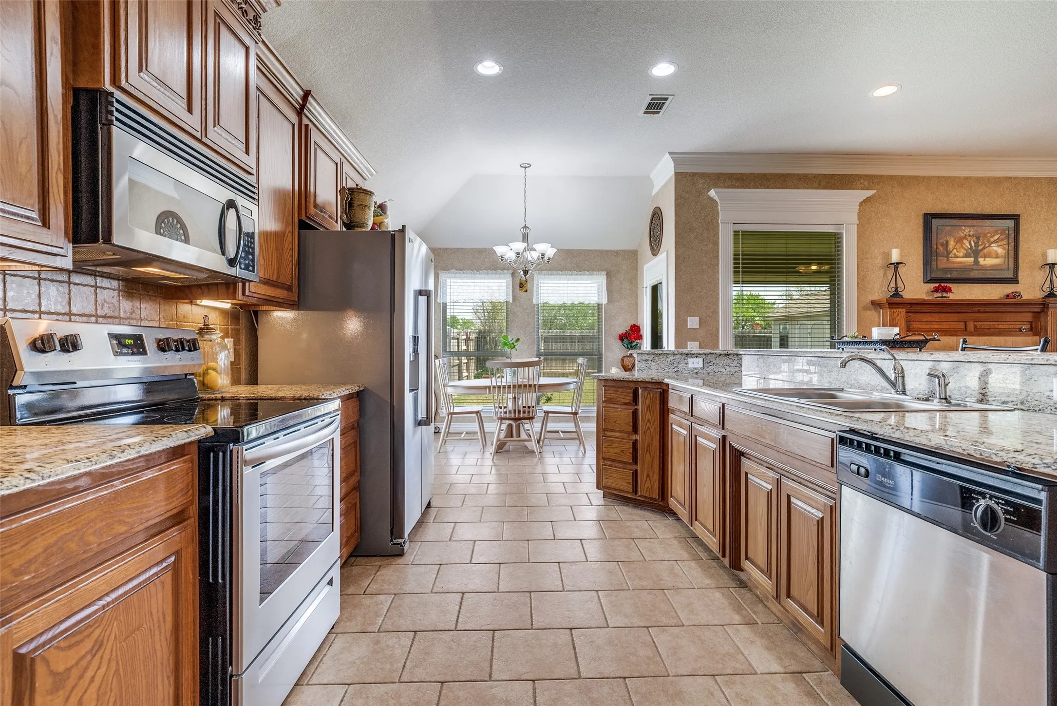 Kitchen with stainless steel appliances, lofted ceiling, a chandelier, light stone countertops, and wood finish cabinetry