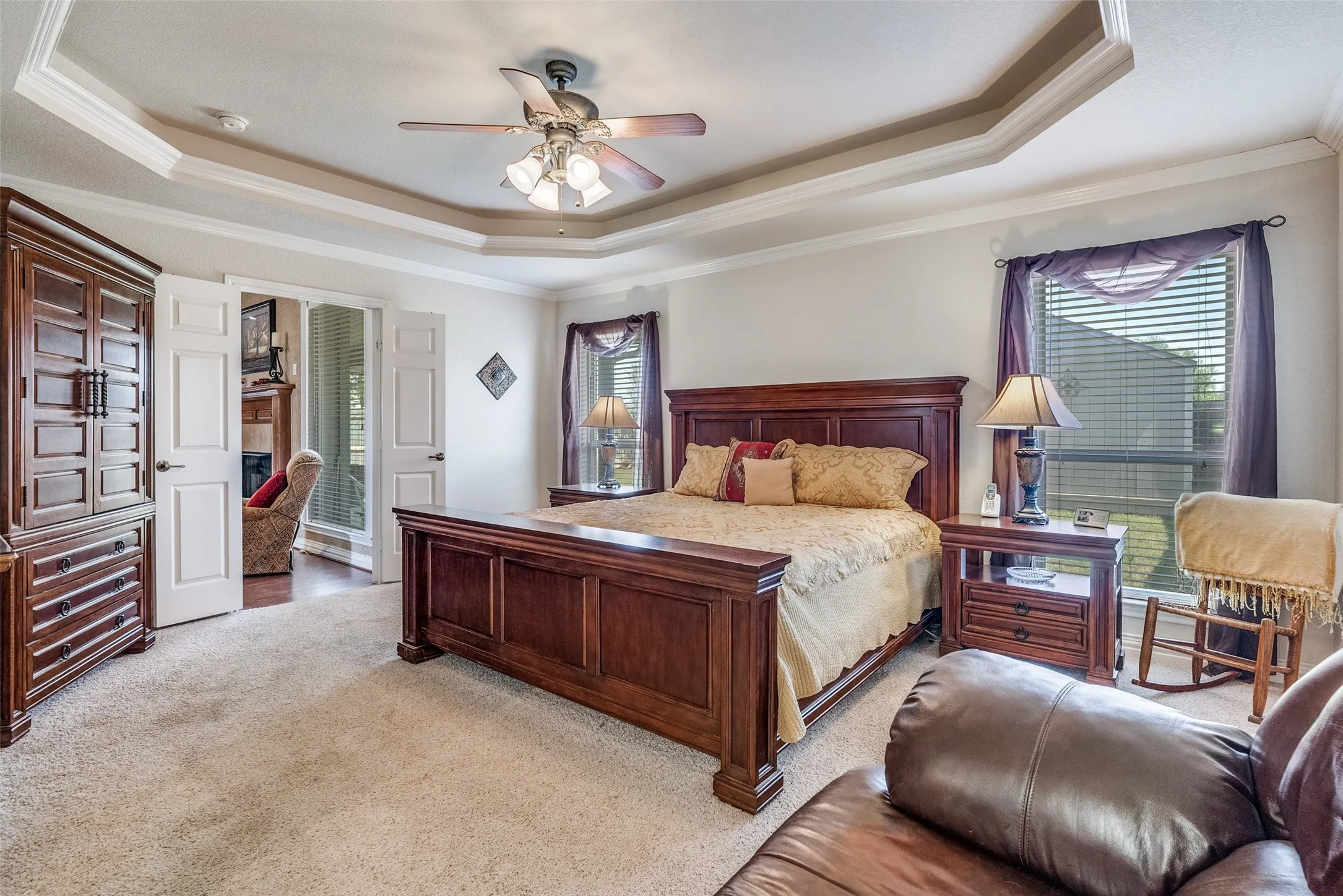 Bedroom with ornamental molding, multiple windows, light carpet, a ceiling fan, and a raised ceiling