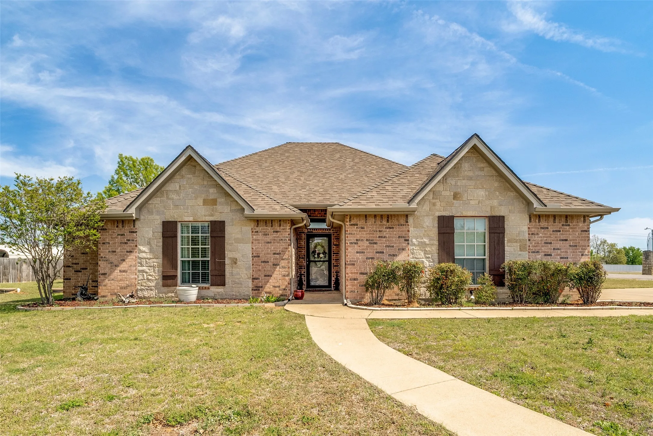 Single story home with a shingled roof, a front lawn, brick siding, and stone siding