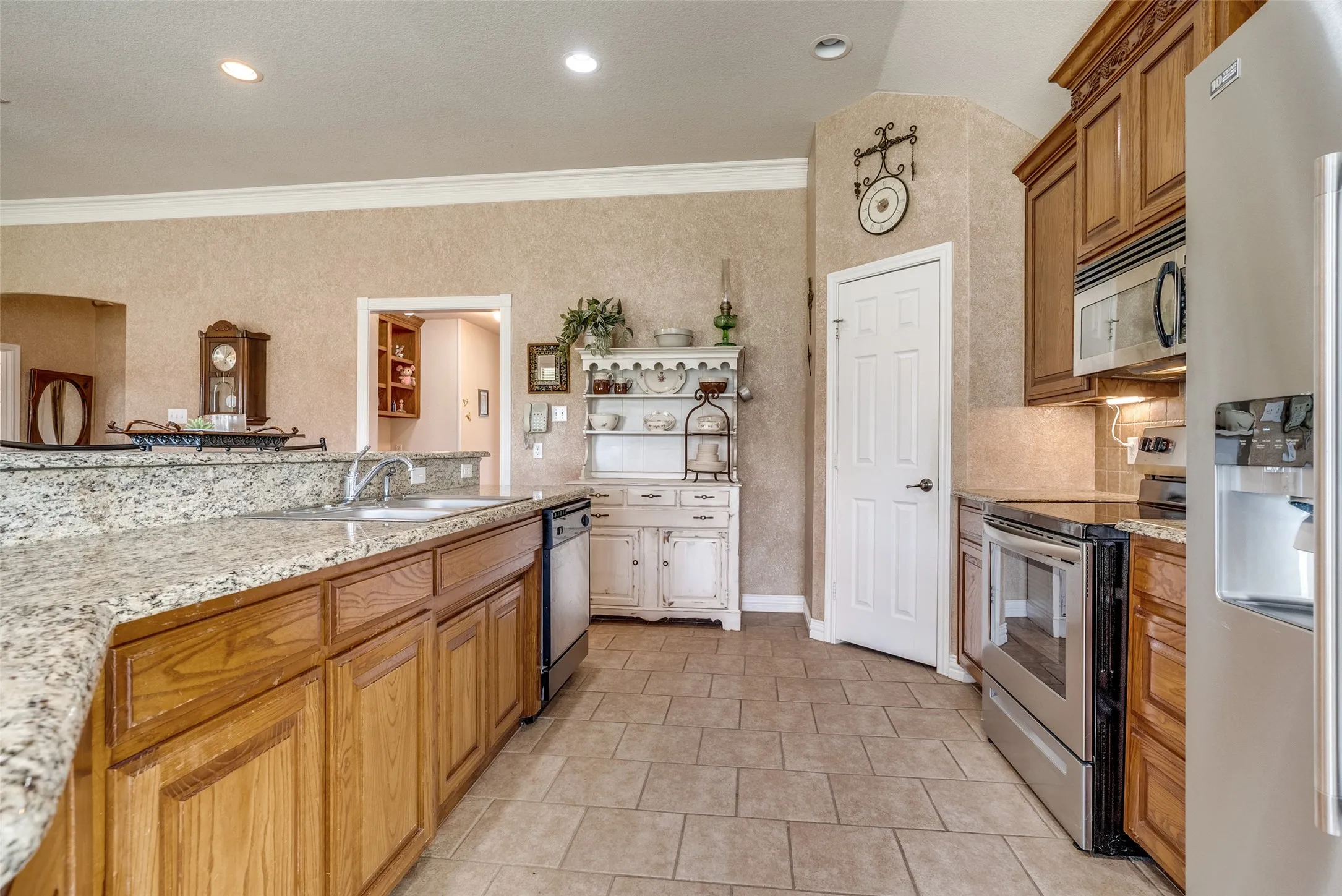 Kitchen featuring stainless steel appliances, wood finish cabinets, light stone counters, crown molding, and open shelves