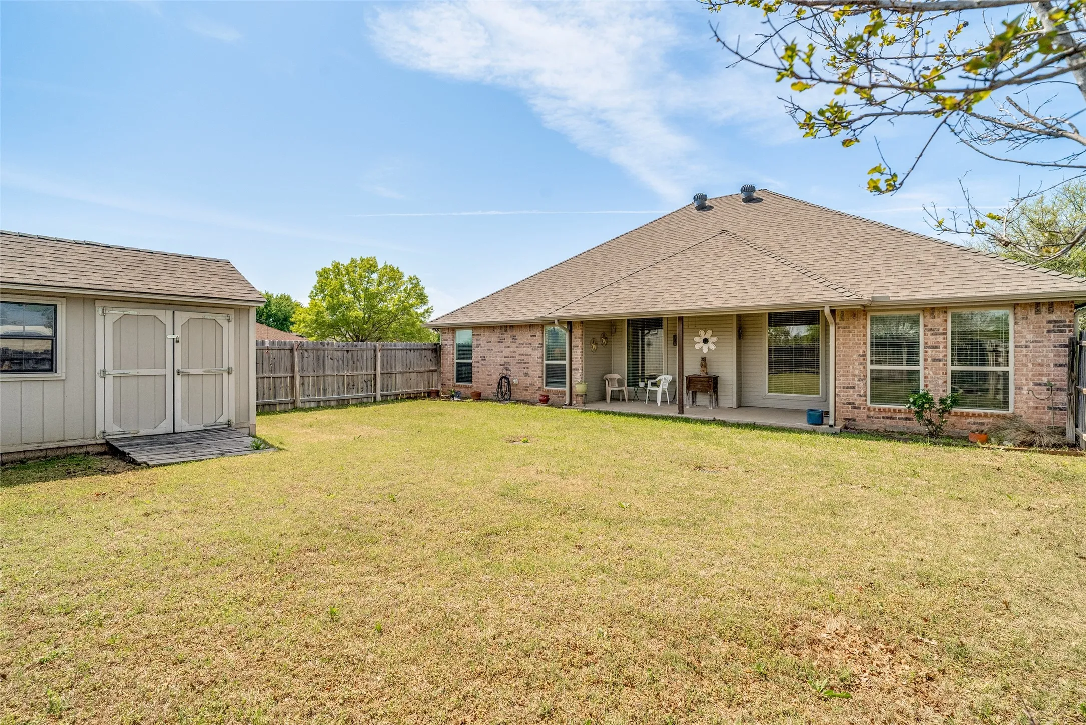 Rear view of property with a storage unit, roof with shingles, brick siding, a fenced backyard, and a patio area