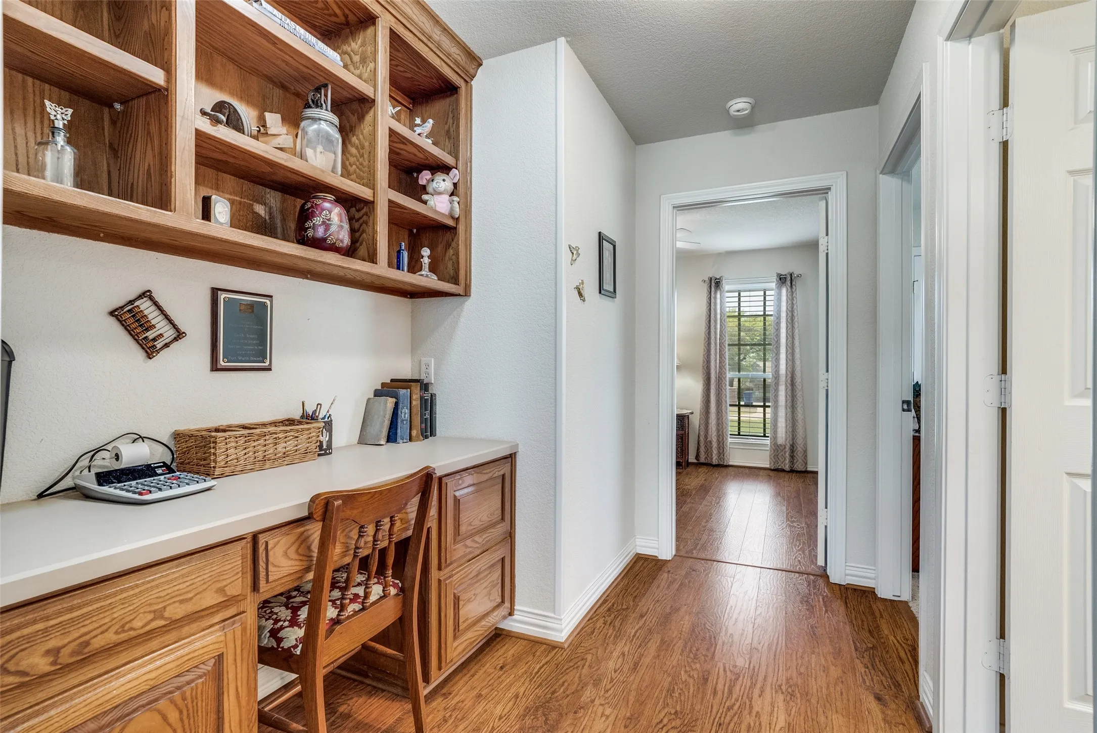 Home office with built in desk, light wood-style floors, and a textured ceiling