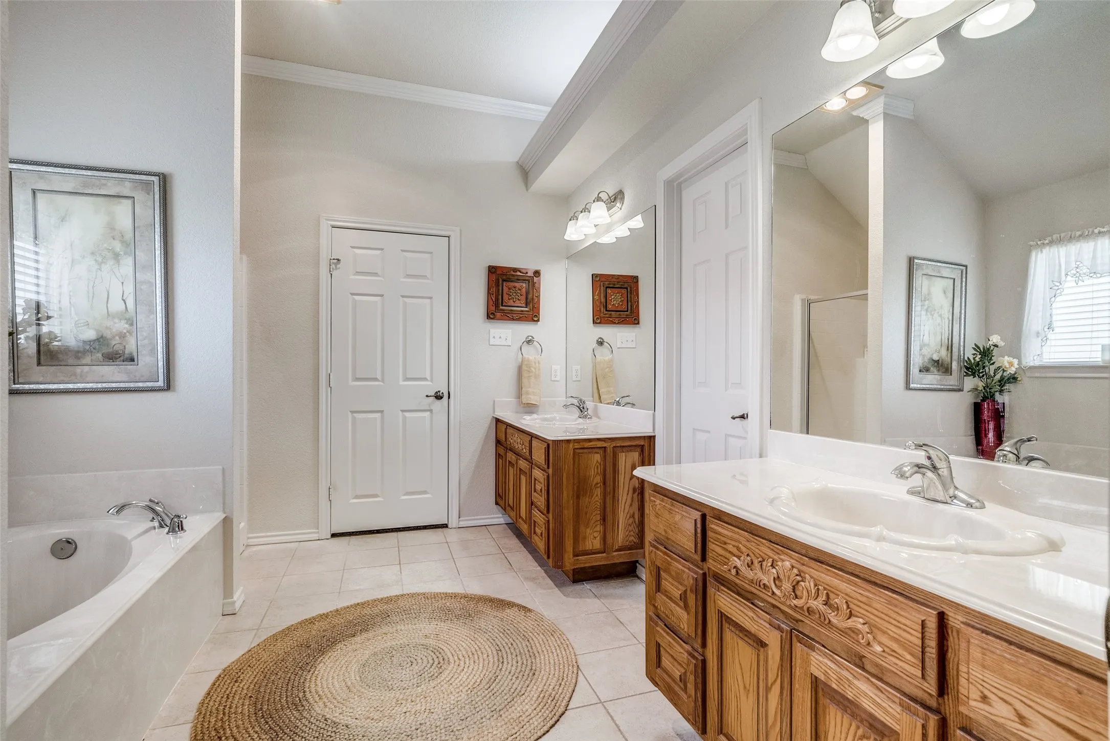 Full bath featuring a bath, two vanities, light tile patterned flooring, and crown molding