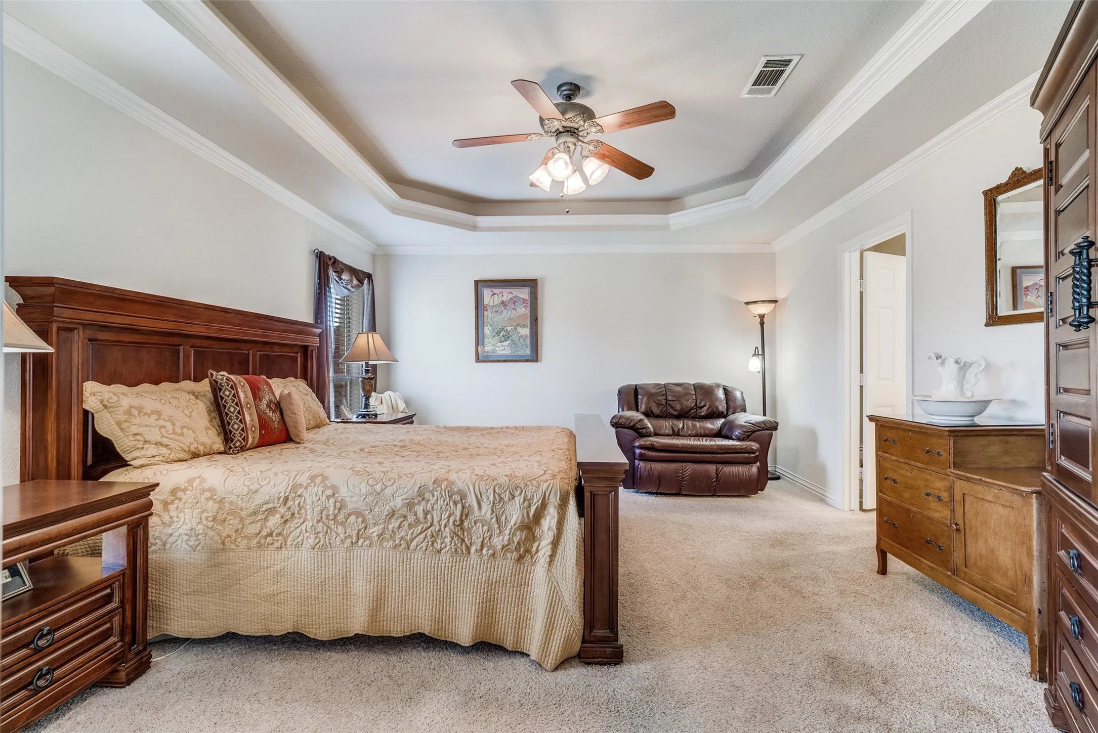 Bedroom with light colored carpet, ornamental molding, ceiling fan, and a raised ceiling