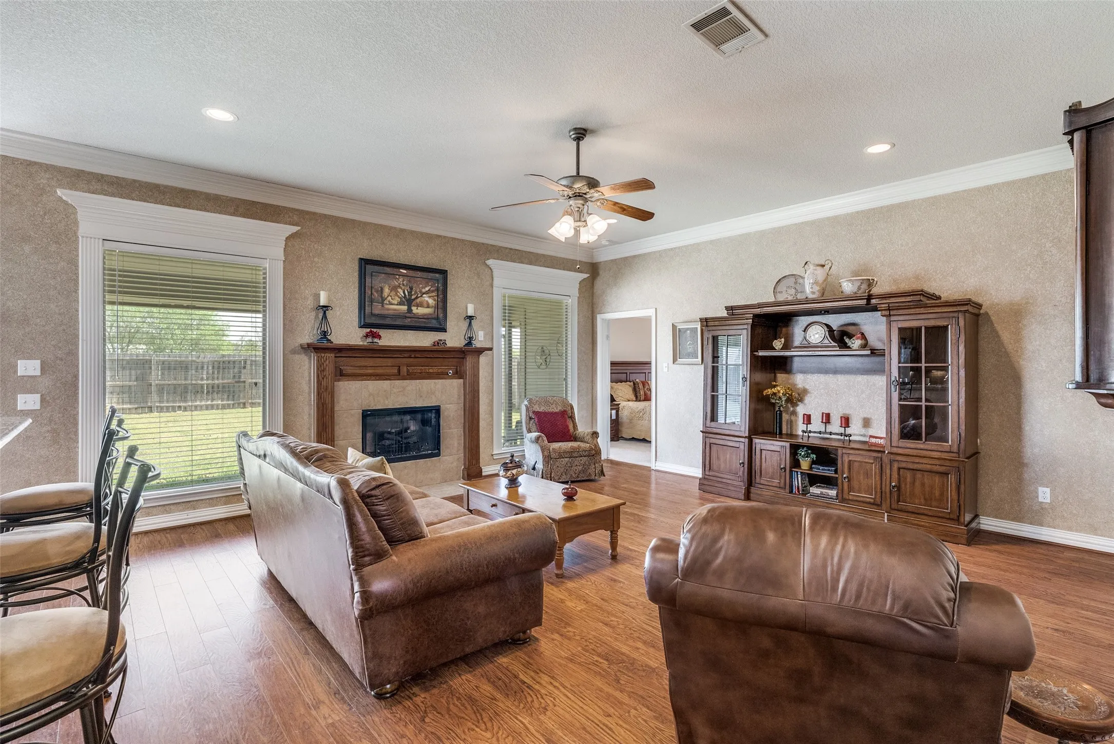 Living area with a fireplace, wood finished floors, a ceiling fan, ornamental molding, and a textured ceiling