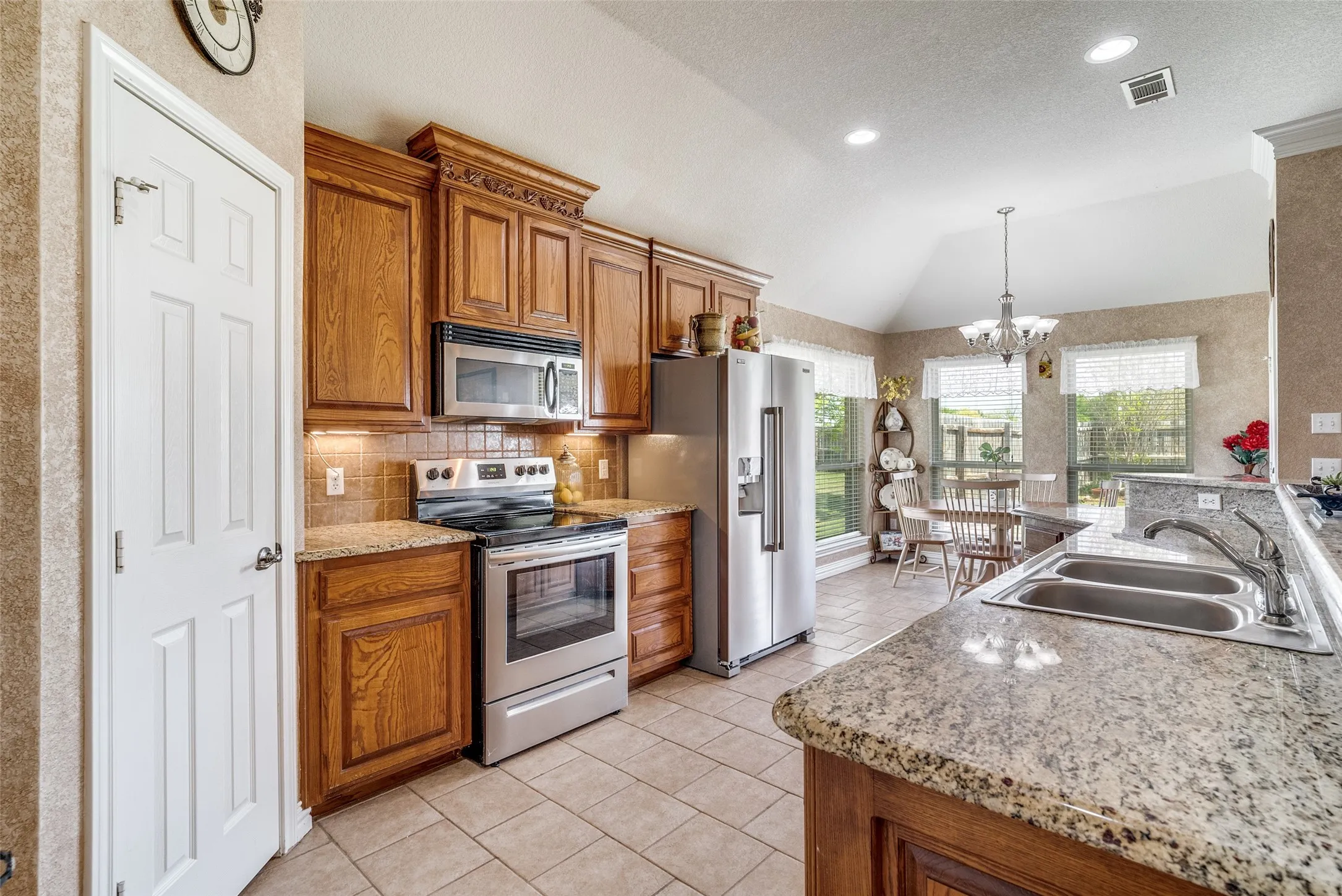 Kitchen featuring wood finish cabinetry, stainless steel appliances, suspended lighting, decorative backsplash, and light stone counters