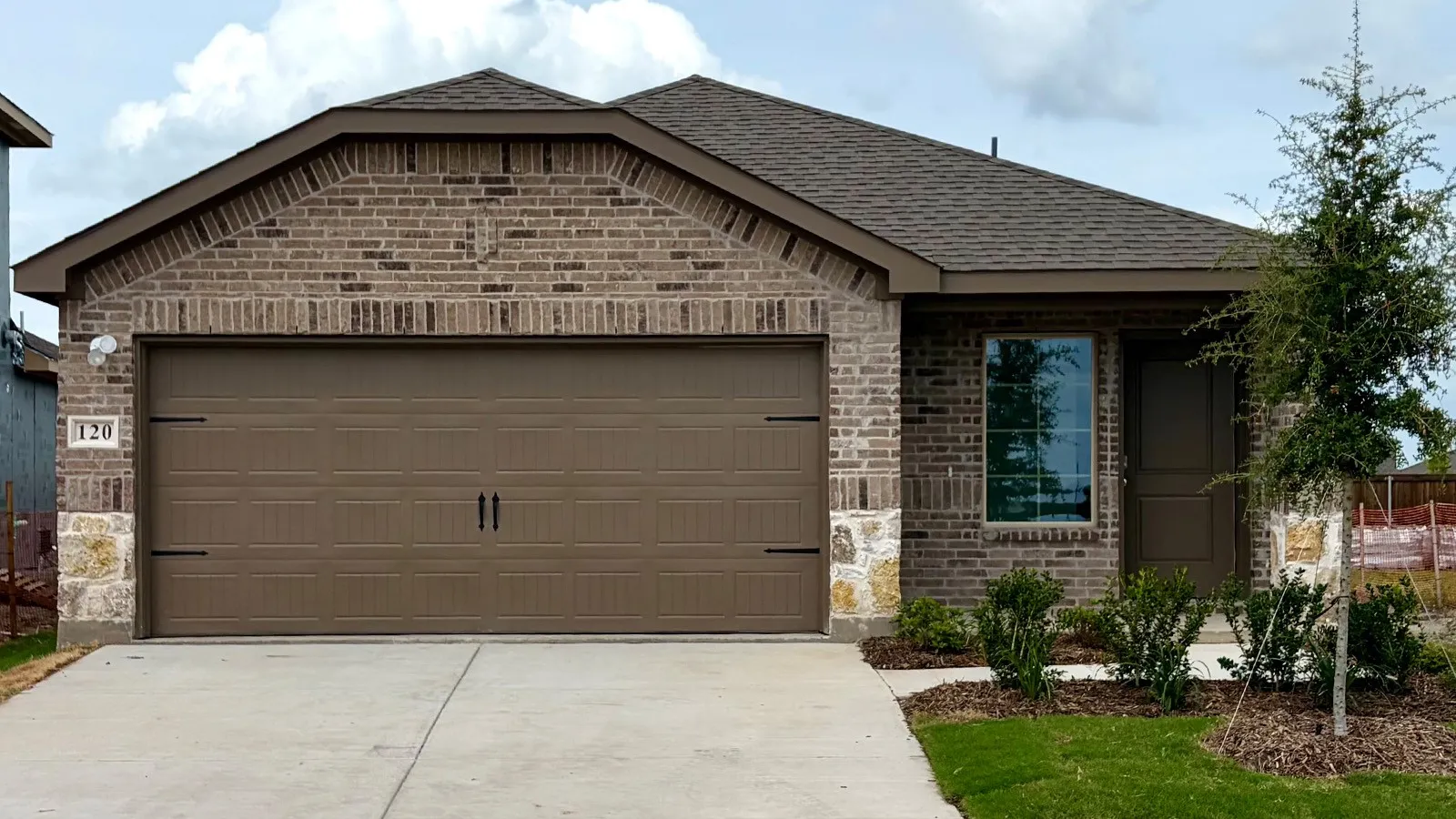 Brick and stone facade residence featuring a two-car garage with decorative hardware, a covered entry, and a pitched shingle roof
