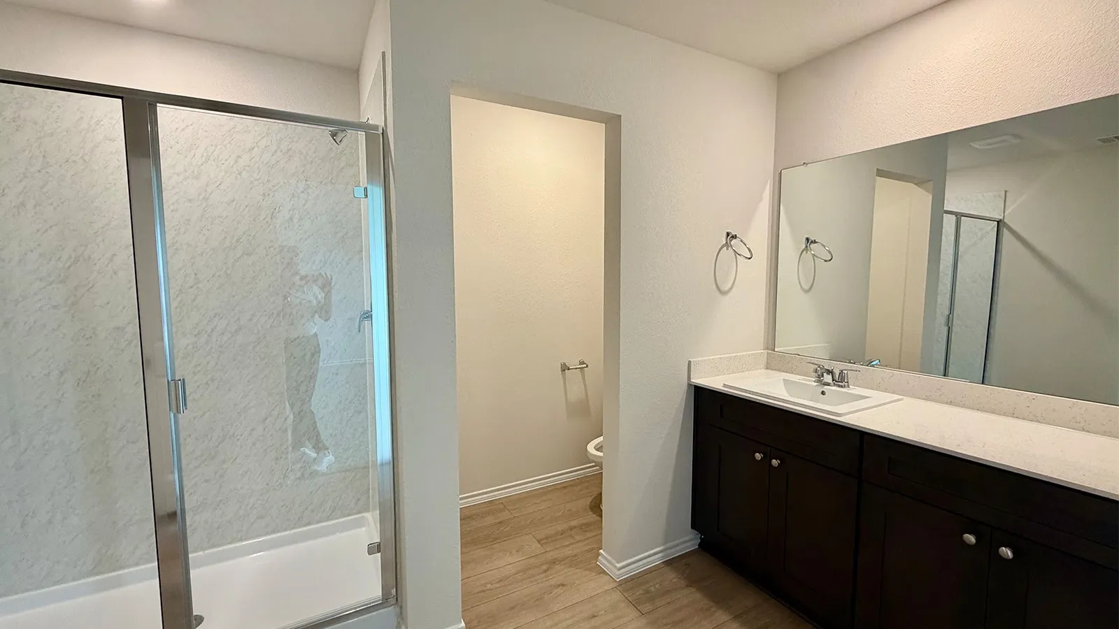 Bathroom featuring a glass-enclosed shower, a double vanity with a light-colored countertop, and dark wood-finish cabinetry