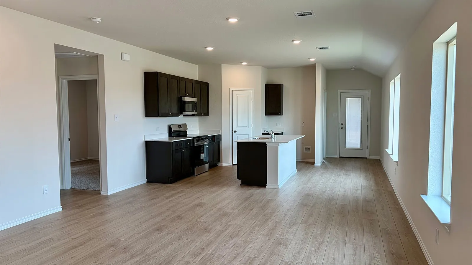 Open-concept kitchen and living area featuring wood-finish flooring, dark wood cabinetry, a central island with white countertops, and stainless steel appliances