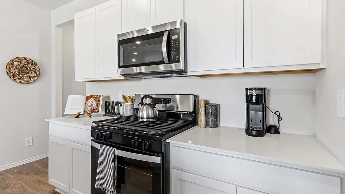 White shaker cabinetry, stainless steel microwave, black gas range, white countertops, and wood-finish flooring