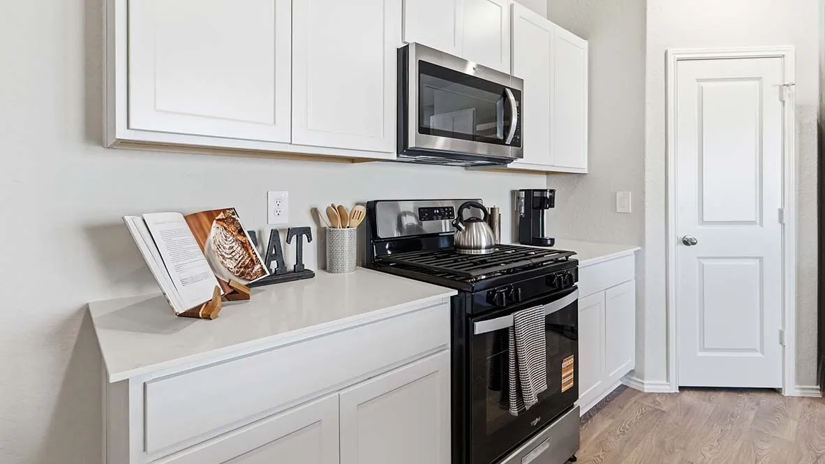 White cabinetry, light-toned countertops, stainless steel microwave, black electric range with stainless steel accents, wood-finish flooring