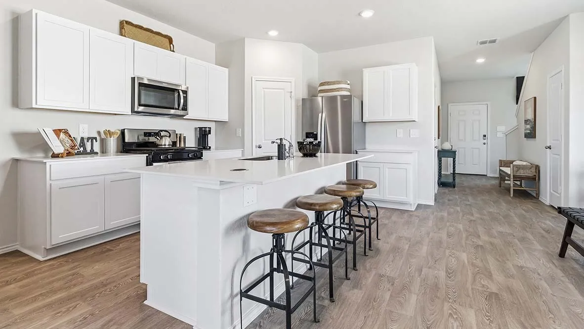 Bright, open-concept kitchen and dining area featuring white cabinetry, stainless steel appliances, a large center island with breakfast bar seating, wood-finish flooring throughout, and recessed lighting