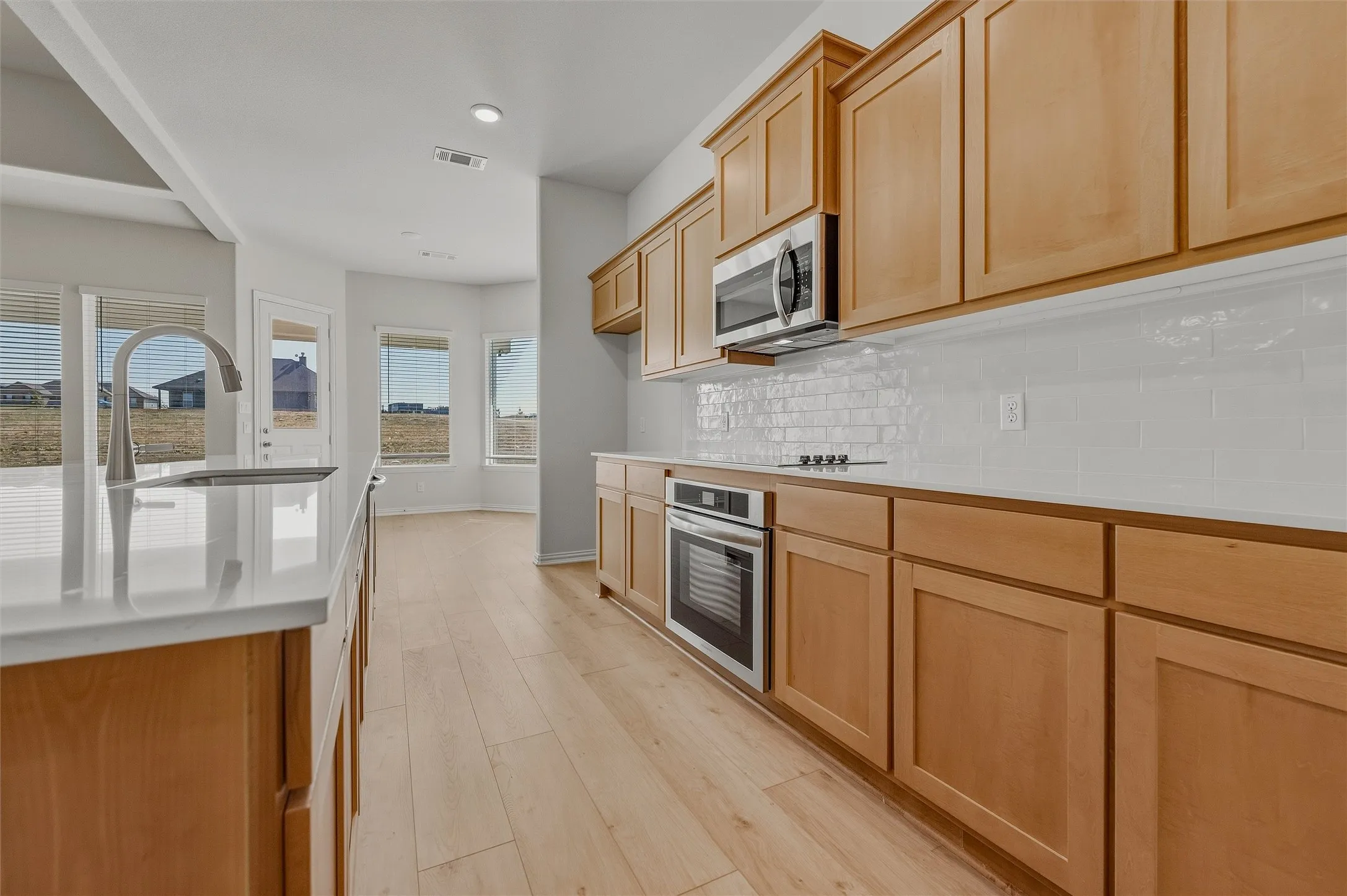 Kitchen featuring light wood-finish cabinetry, white subway tile backsplash, stainless steel appliances, and light wood-finish flooring
