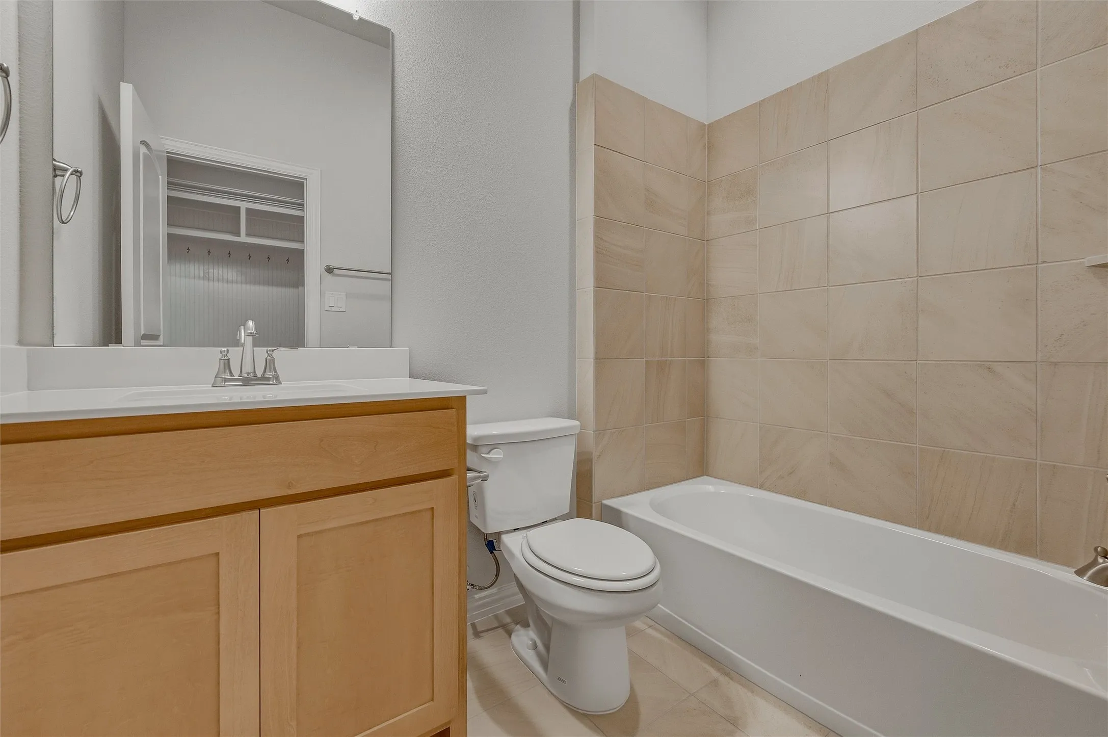 Bathroom featuring a light wood-finish vanity, white countertop with integrated sink, chrome faucet, and tiled shower surround