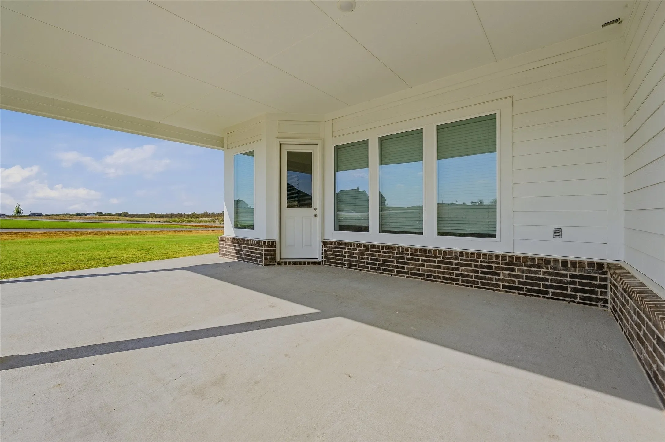 Expansive covered patio with concrete flooring, white siding, and a partial brick facade