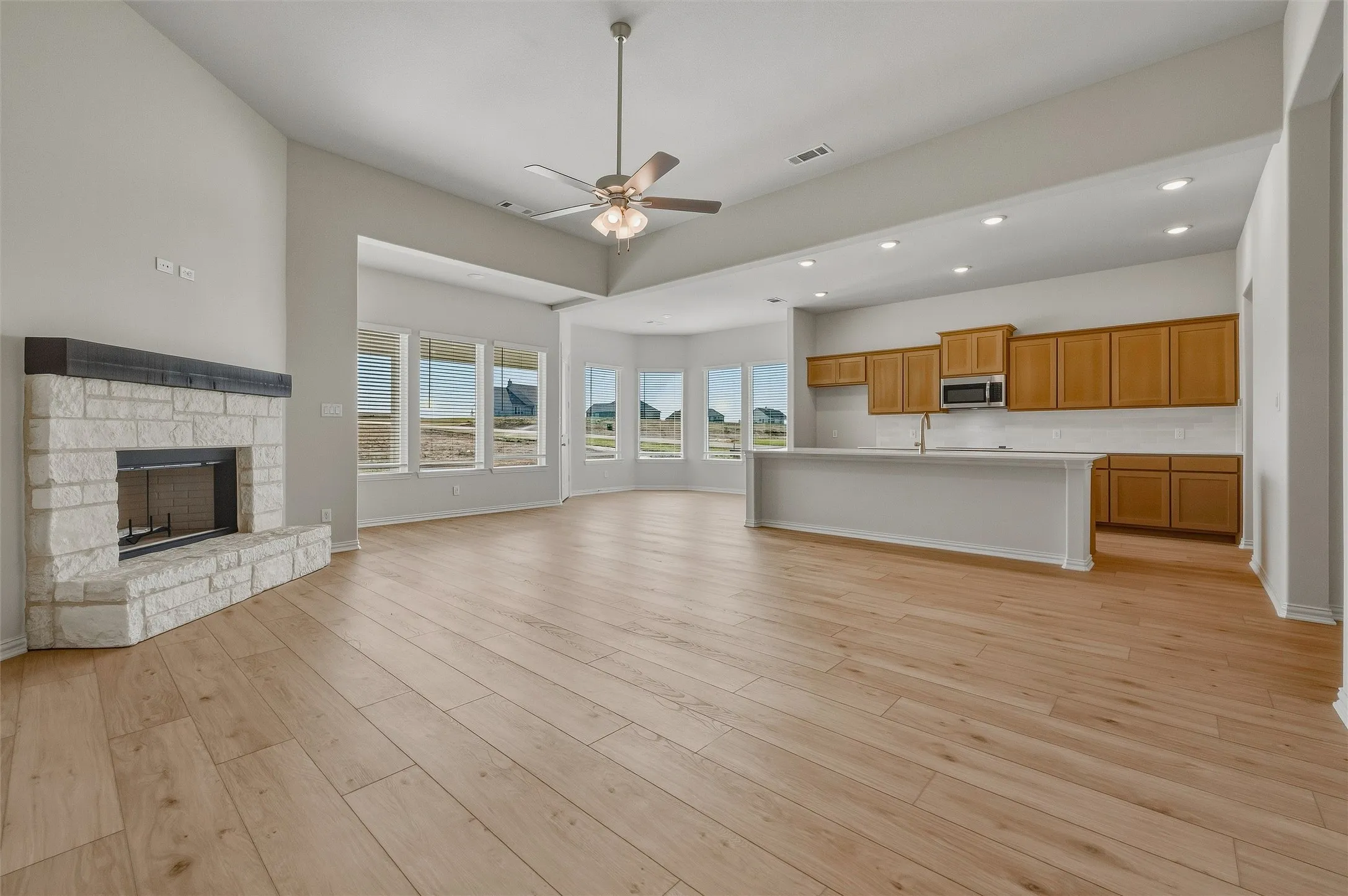Open-concept living area featuring wood-finish flooring, a stone-surround fireplace, and a kitchen island with seating