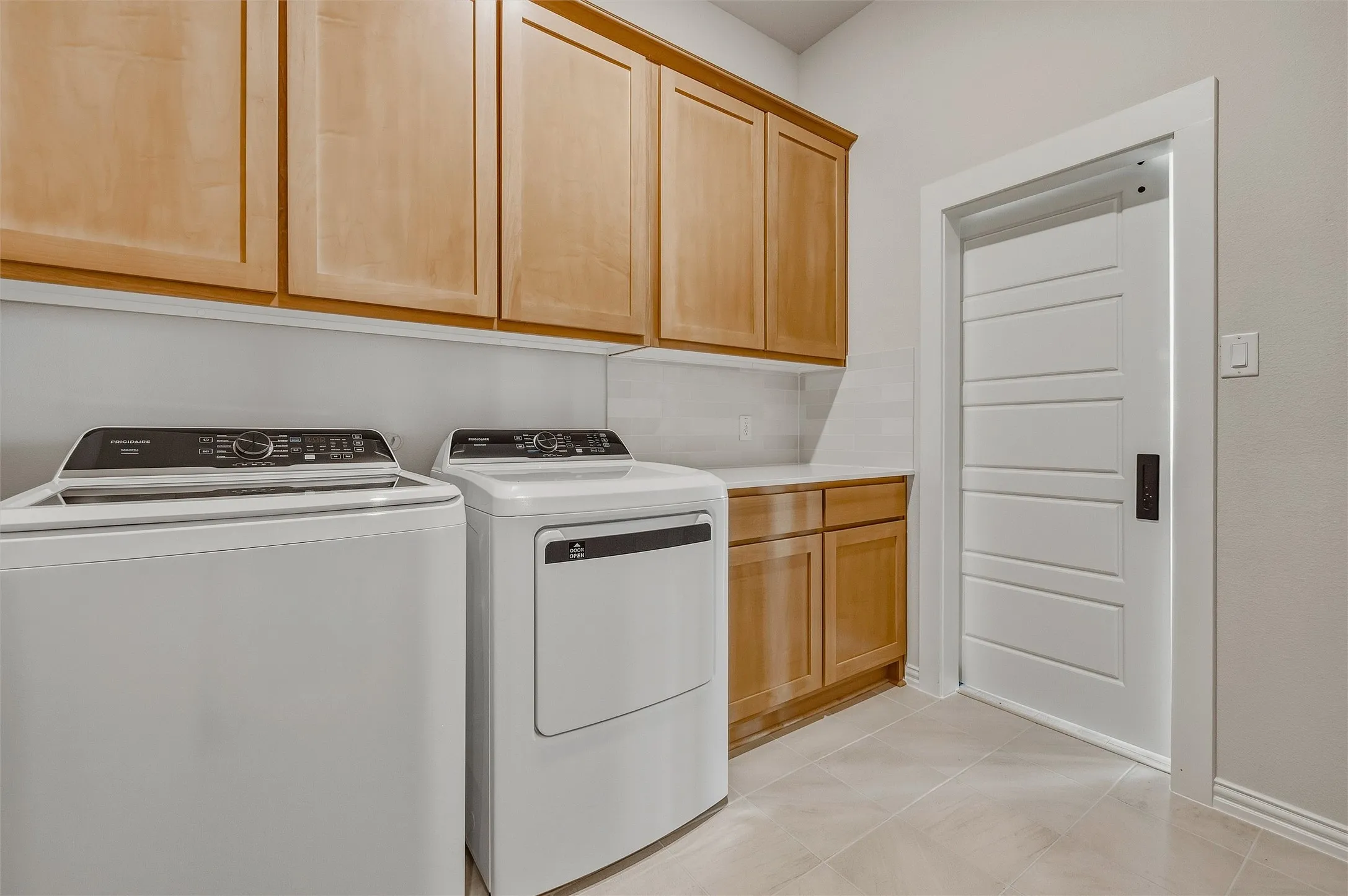 Light wood-finish cabinetry, tile flooring, and a contemporary panel door with a dark finish handle