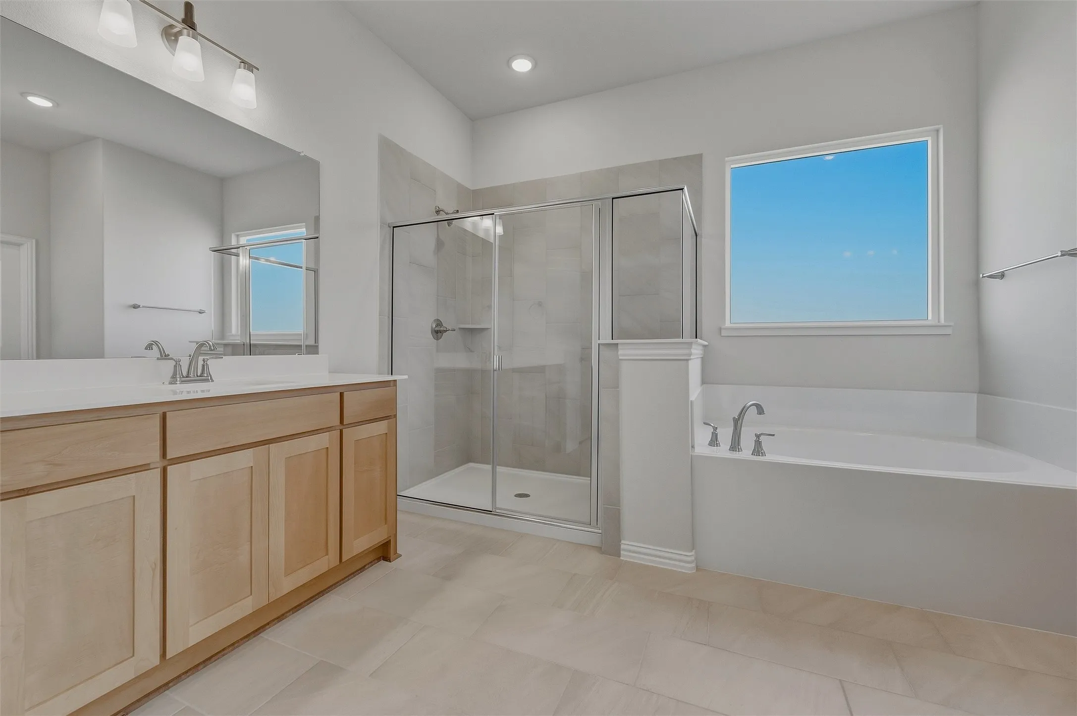 Spacious bathroom featuring a built-in soaking tub, a separate glass-enclosed shower, a double vanity with light wood cabinetry, and a large wall-mounted mirror