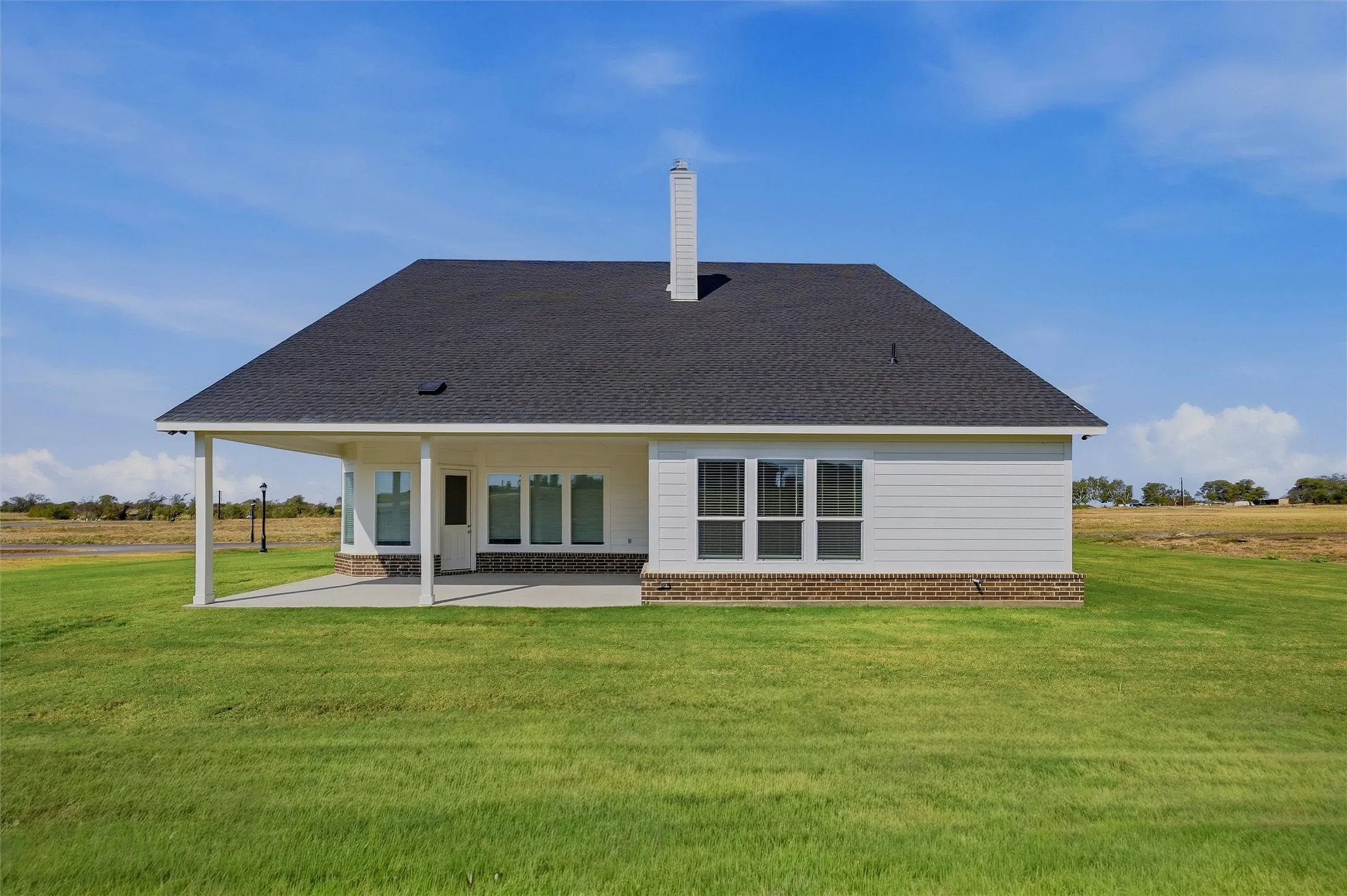 Expansive rear yard featuring a covered patio, broad shingle roof, and durable siding with brick accents