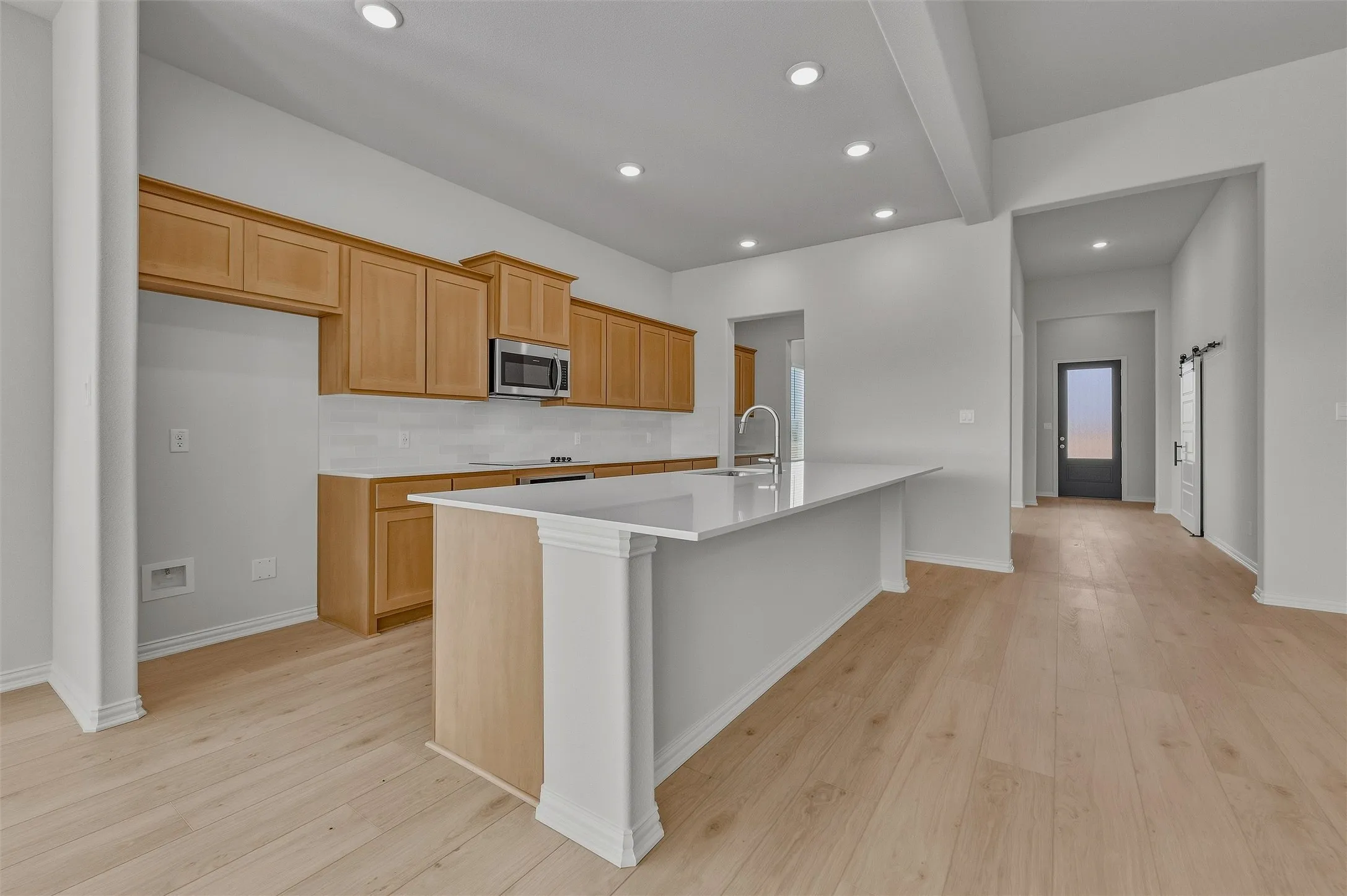 Kitchen featuring light wood-finish cabinetry, white subway tile backsplash, white countertop, and stainless steel microwave