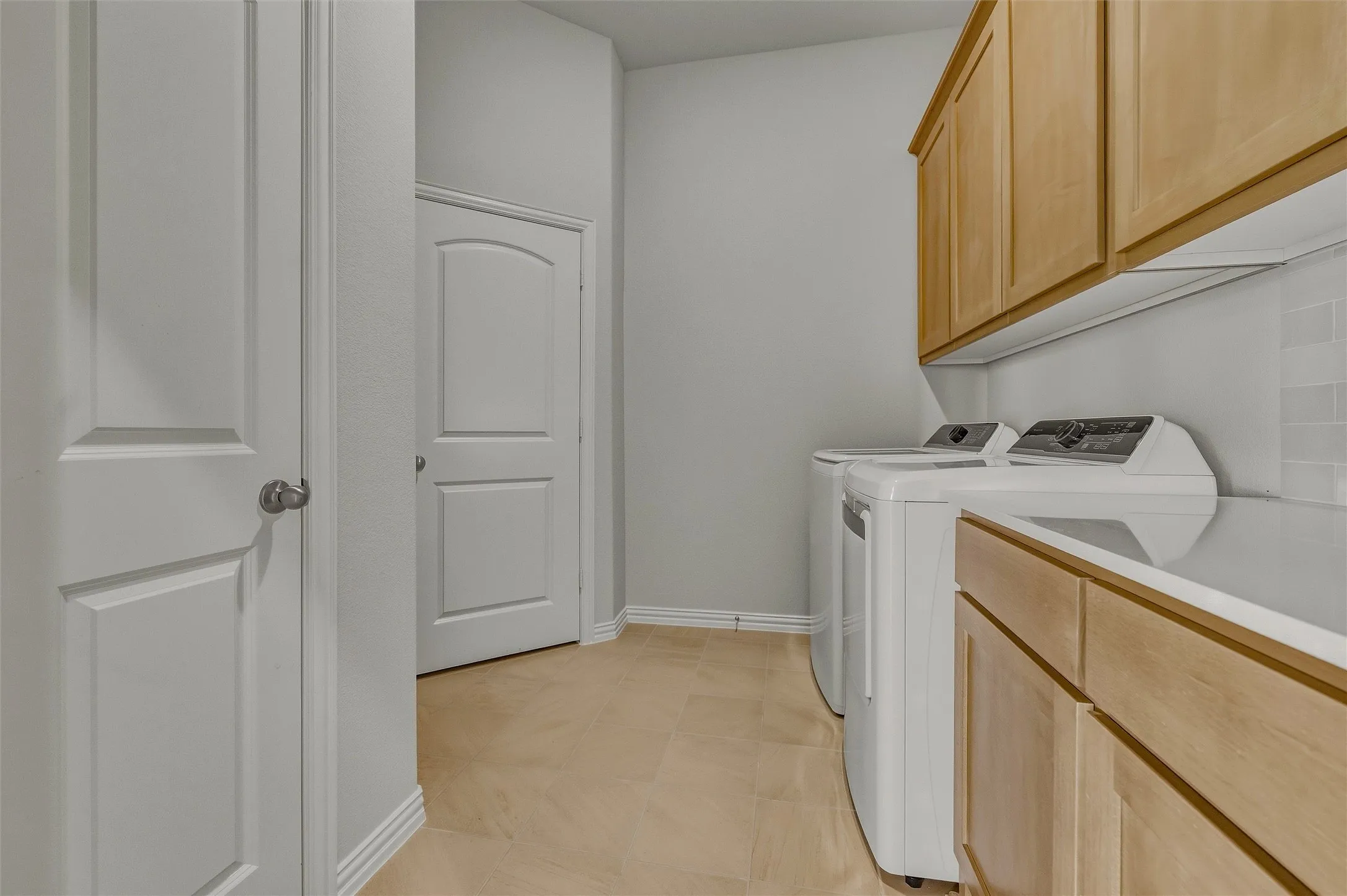 Light wood cabinetry, light countertop, subway tile backsplash, and light-colored flooring