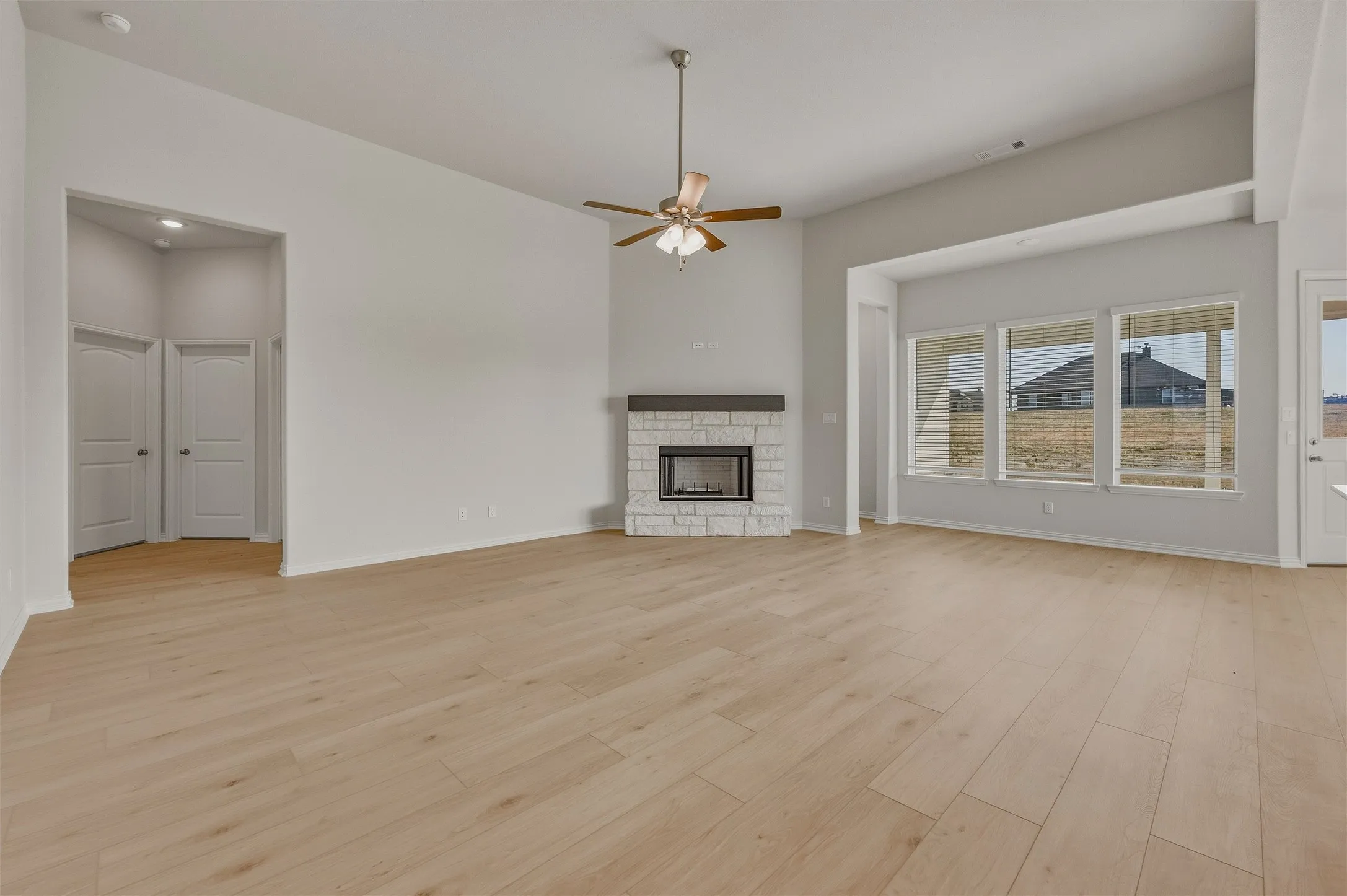 Spacious room featuring wood-finish flooring, a stone-clad fireplace, a ceiling fan, and multiple windows