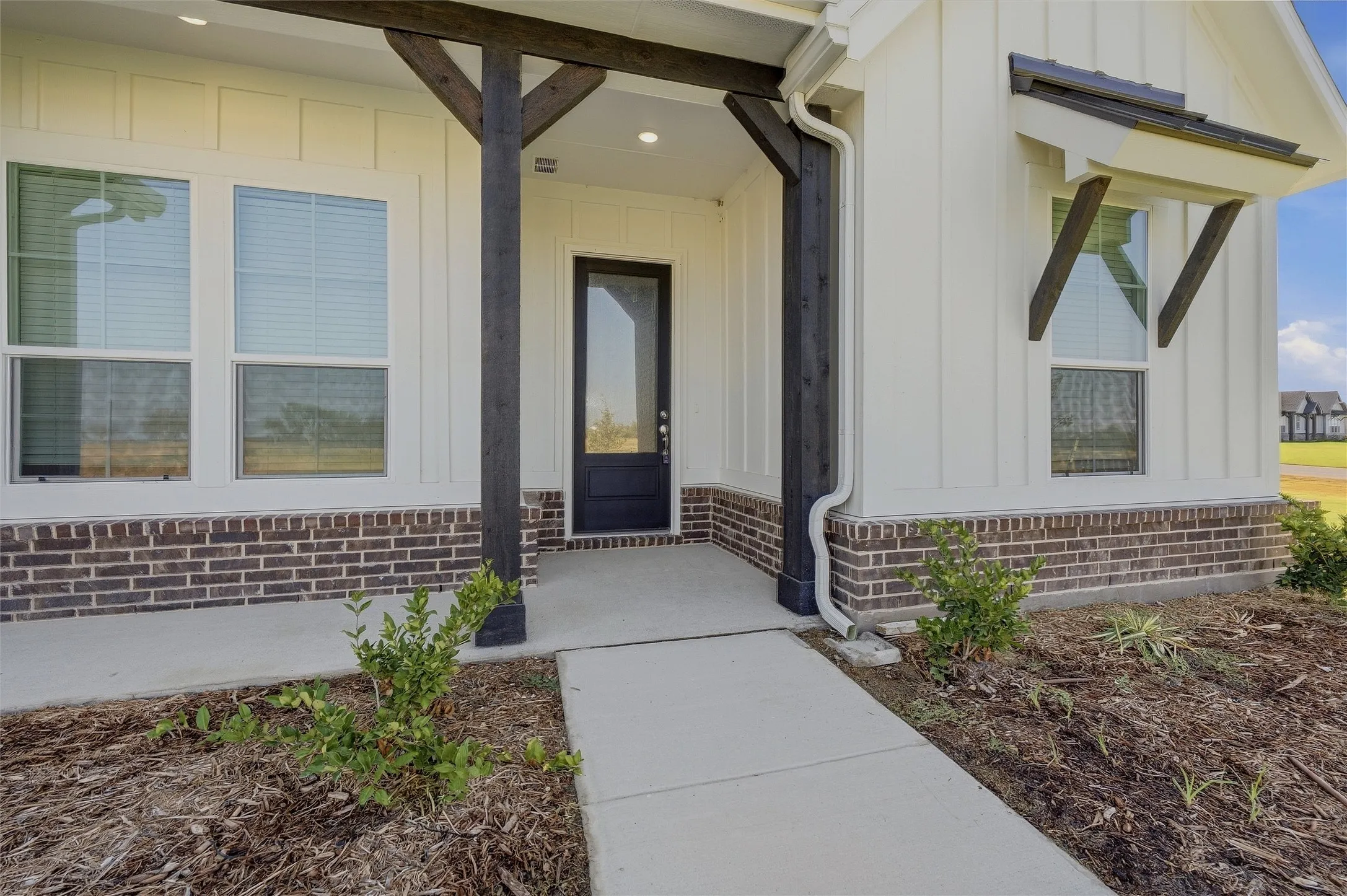 White board and batten siding, dark brick foundation, and a concrete pathway