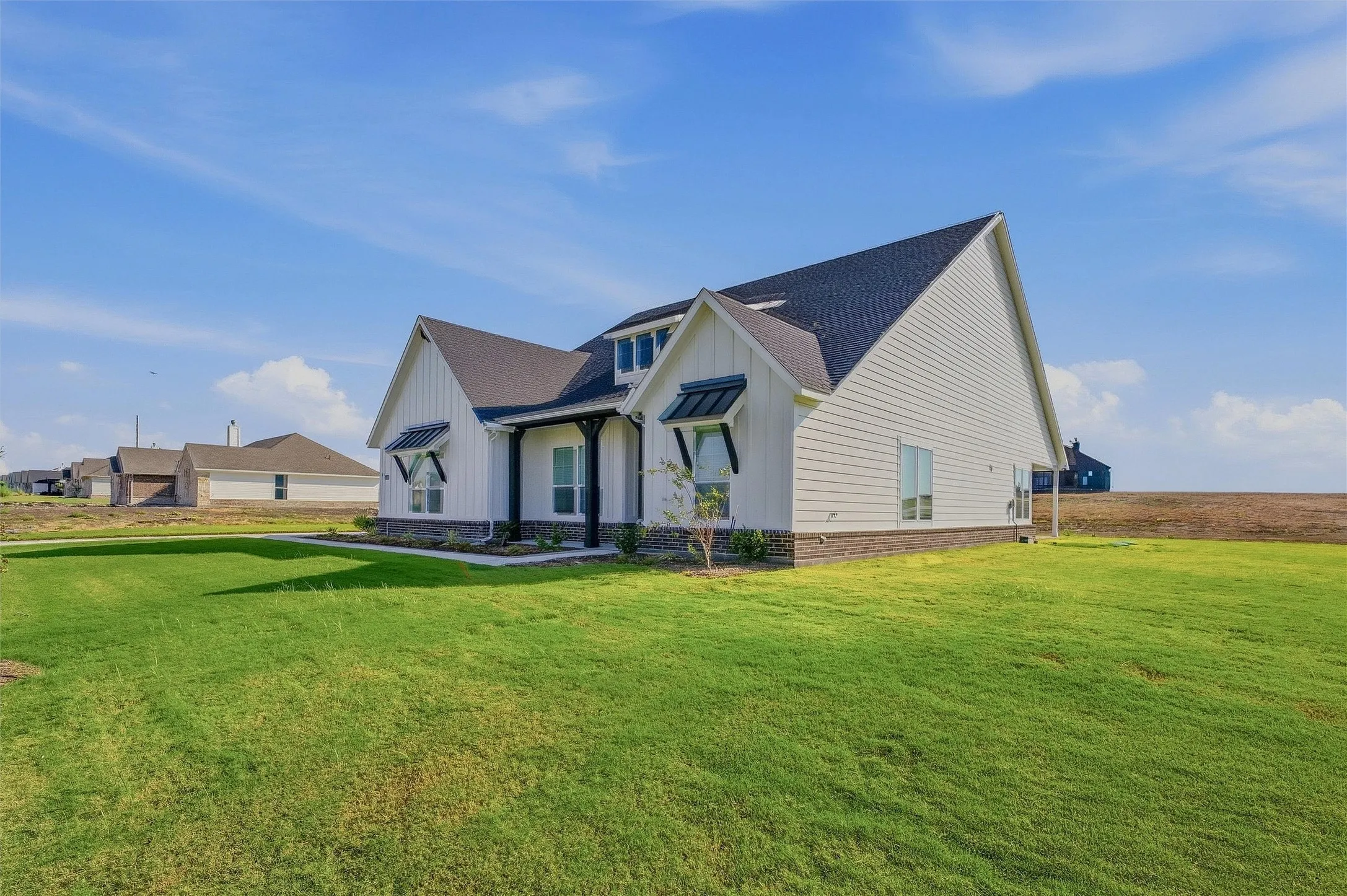 White siding exterior with a dark shingle roof, stone foundation, and black accent awnings