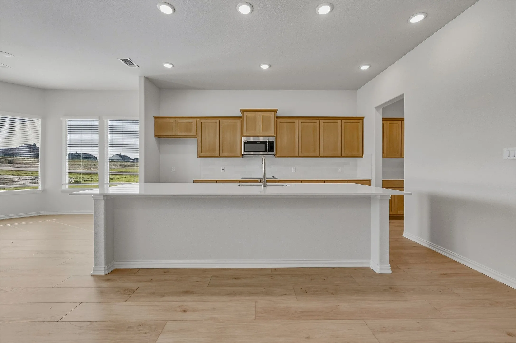 Open-concept living space with wood-finish flooring, recessed lighting, and a kitchen island featuring a stainless steel sink