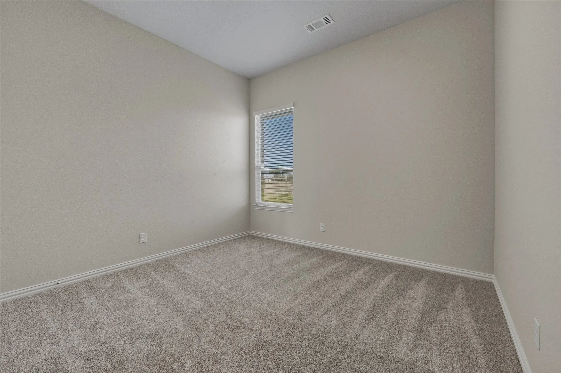 Neutral wall paint, carpet flooring, and a single window with horizontal blinds