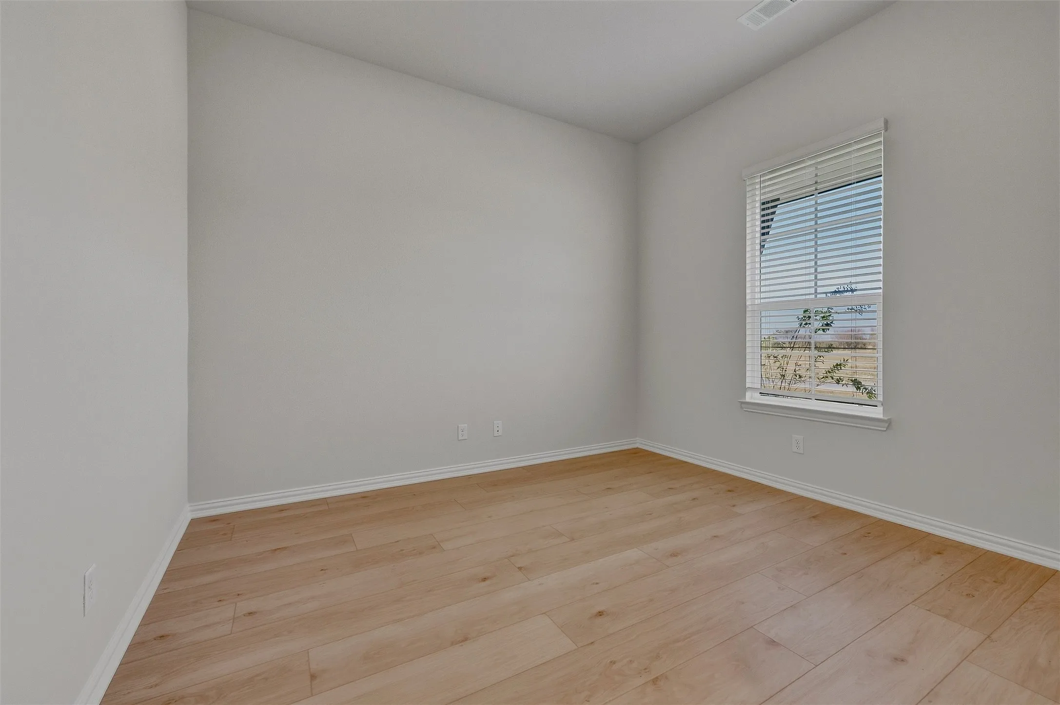 Wood-finish flooring with white trim, a single window with blinds, and light-toned walls