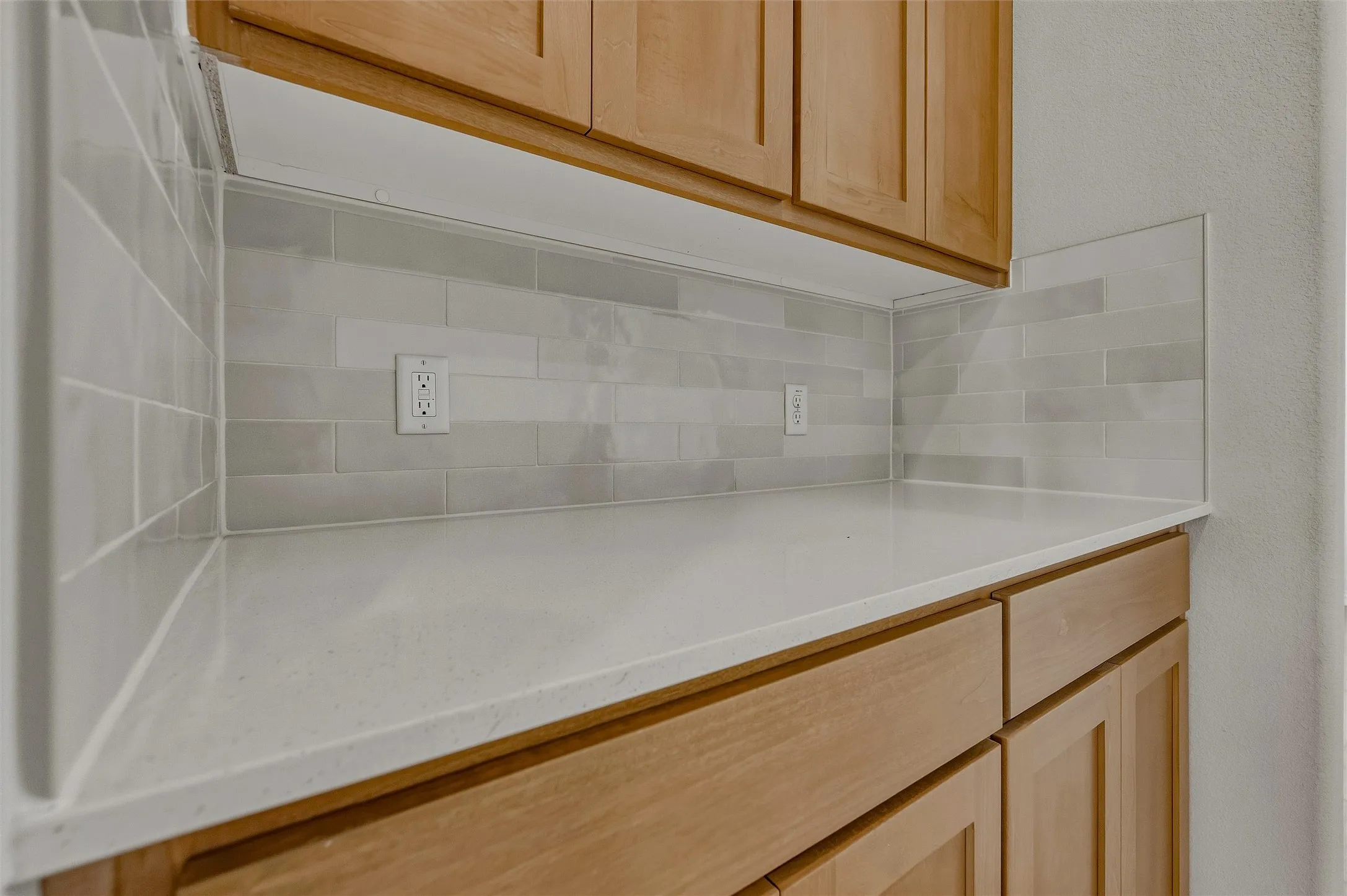 Light wood-finish cabinetry with white countertops and a tiled backsplash