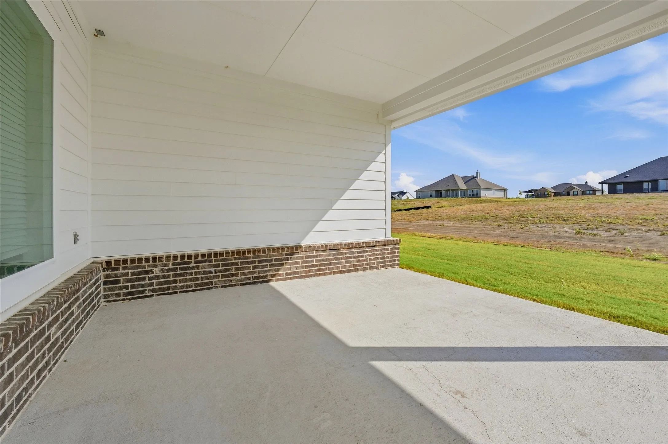 Covered outdoor patio with a concrete surface, featuring a white siding exterior and a brick foundation