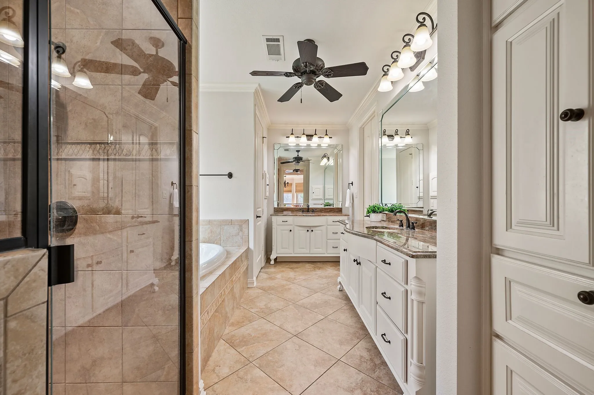 Primary bathroom with dual vanities, a jetted tub, separate shower, and tile flooring.