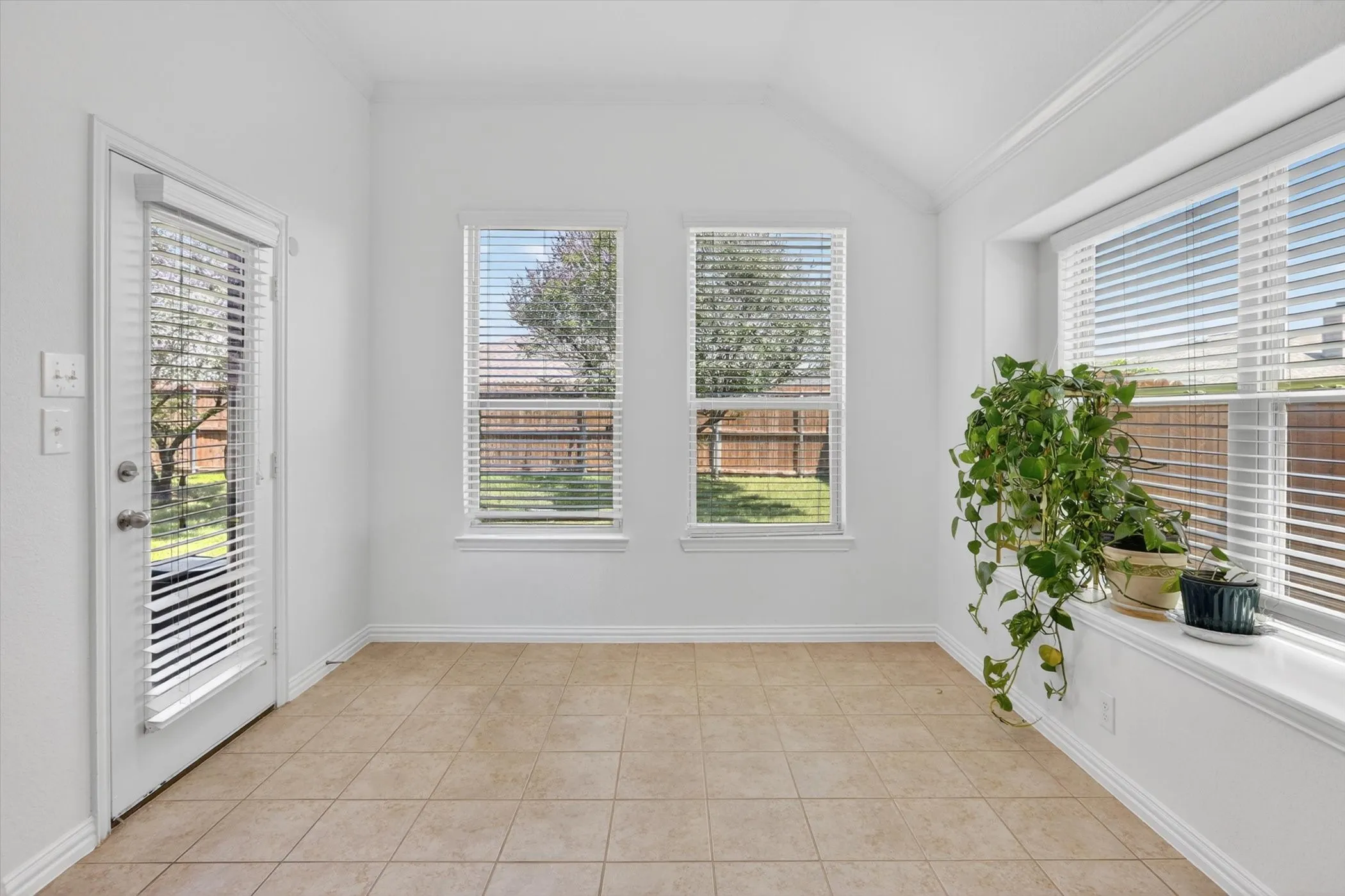 Spacious room featuring tile flooring, white baseboards, and a vaulted ceiling